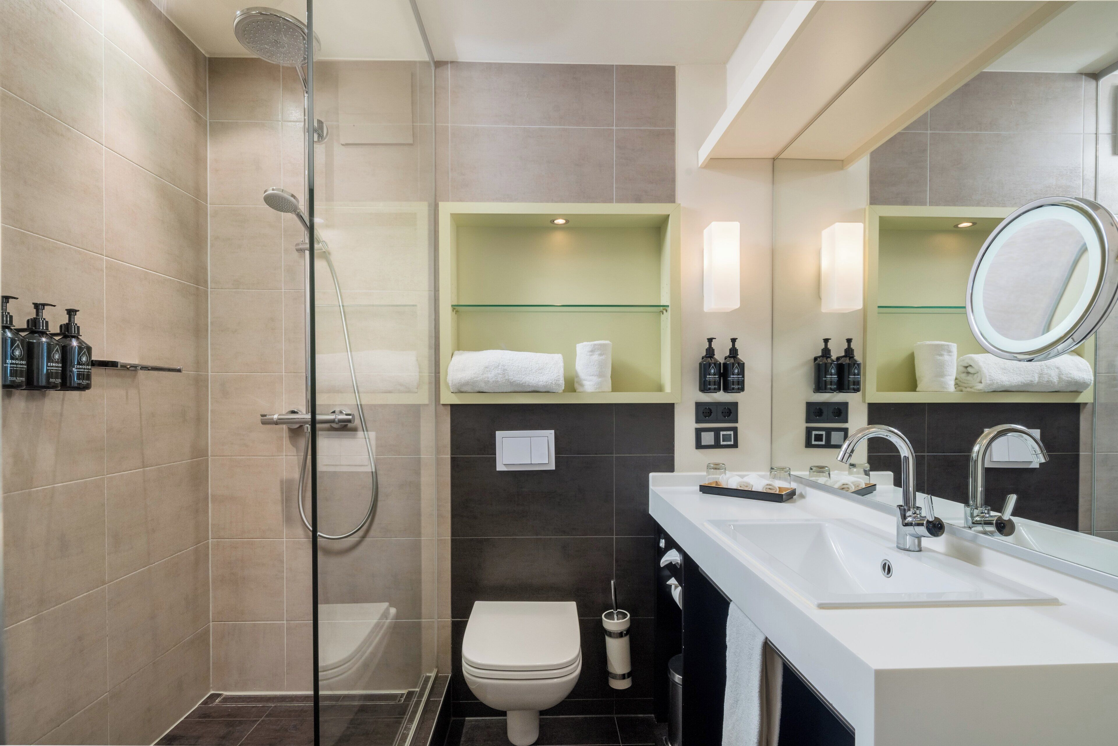 A modern bathroom with a glass-enclosed shower, a white toilet, a sink with a mirror, and toiletries on the countertop.
