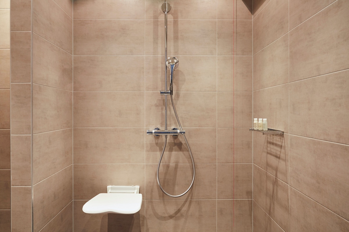 Een douche met een handdouche en een wandmengkraan, een wit toilet en een plank met toiletartikelen.
