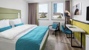 Une chambre d’hôtel avec un lit, un bureau avec une chaise, une lampe et une fenêtre donnant sur des immeubles.