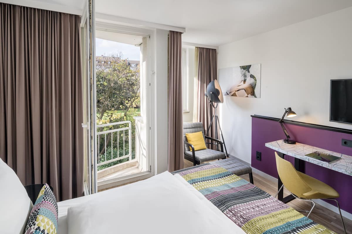 A hotel room with a bed, a desk, a chair, and a view of the outdoors.