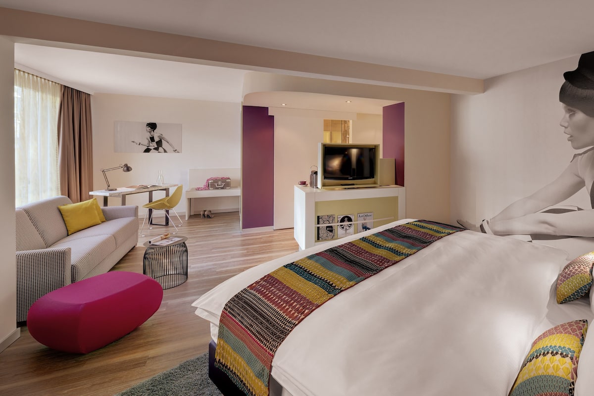 A modern hotel room with a large bed, a sofa, a small table, and a TV.