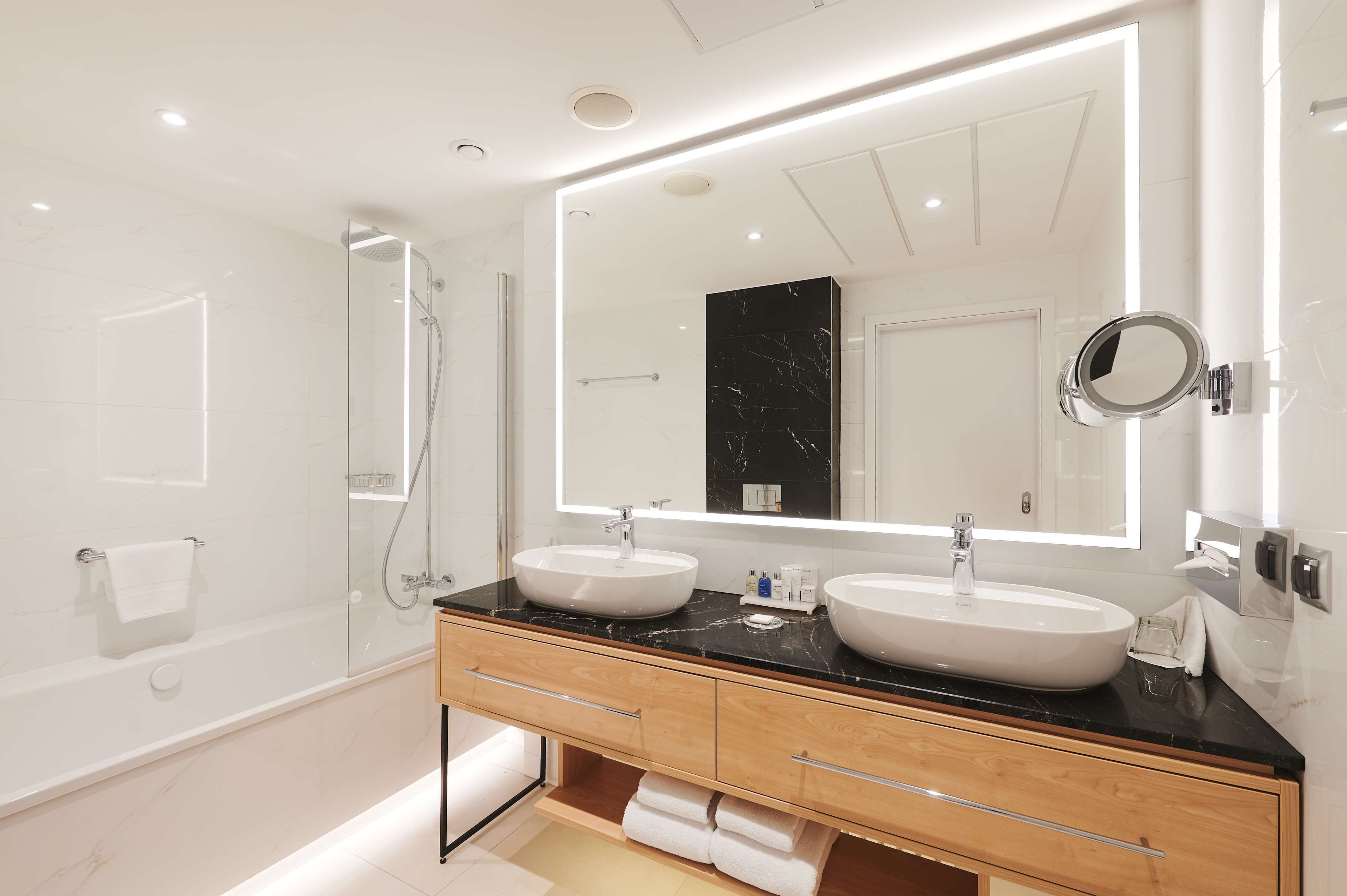 A modern bathroom with two sinks, a large mirror, and a glass-enclosed shower.