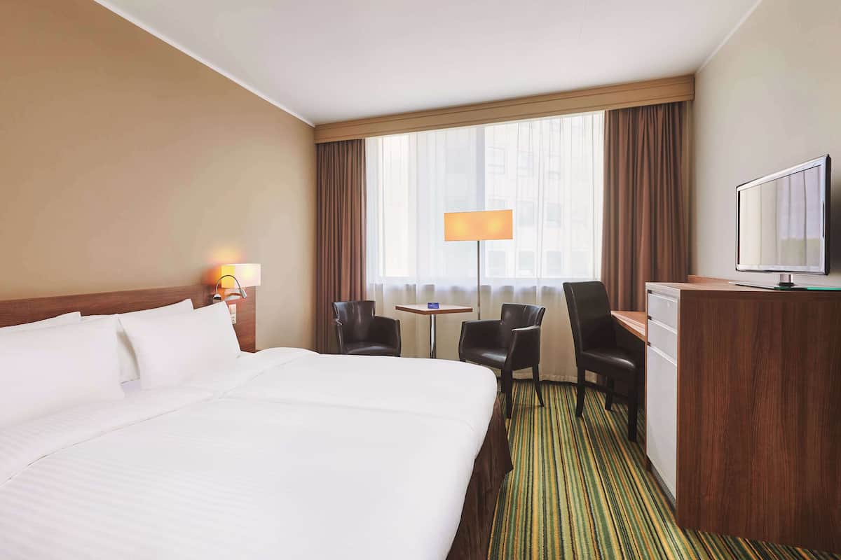 A hotel room with a large bed, a desk with a television, two chairs, a small table, and a window with curtains.