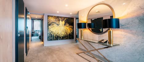 A modern hotel lobby with a marble wall, a large abstract painting, a glass console table with a phone, and a circular mirror.