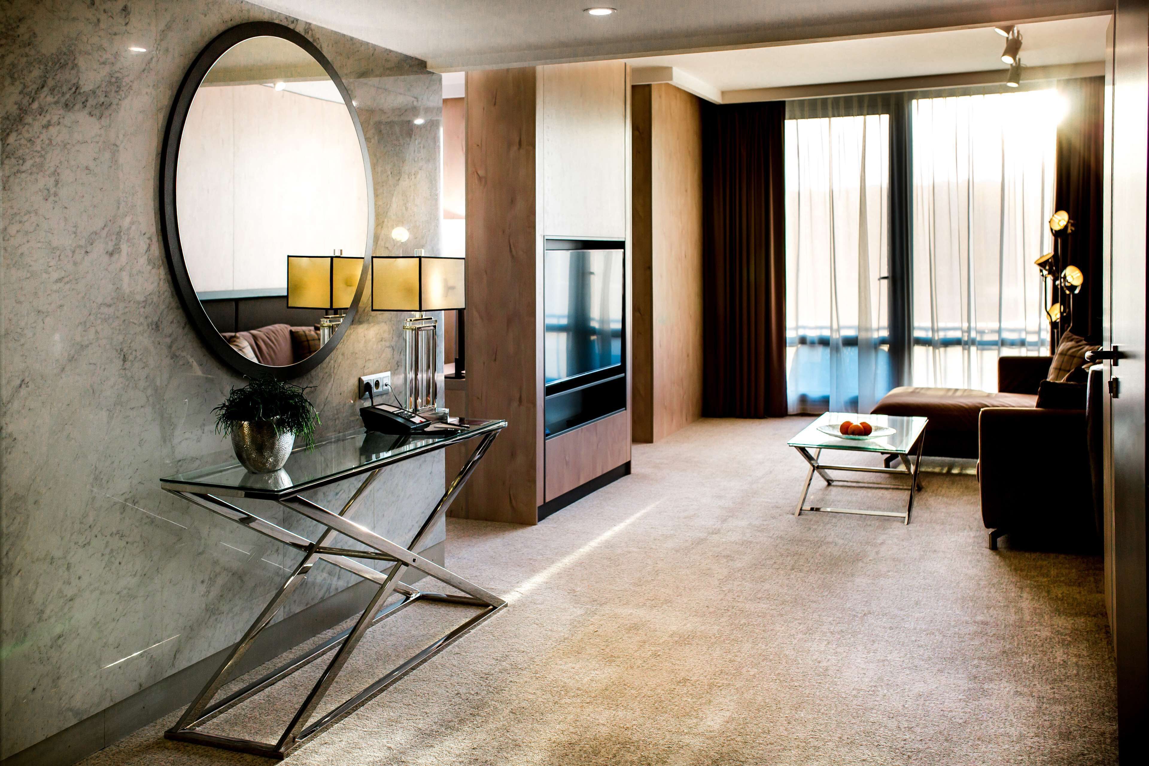 A modern living room with a glass coffee table, a sofa, a TV, and a large mirror.