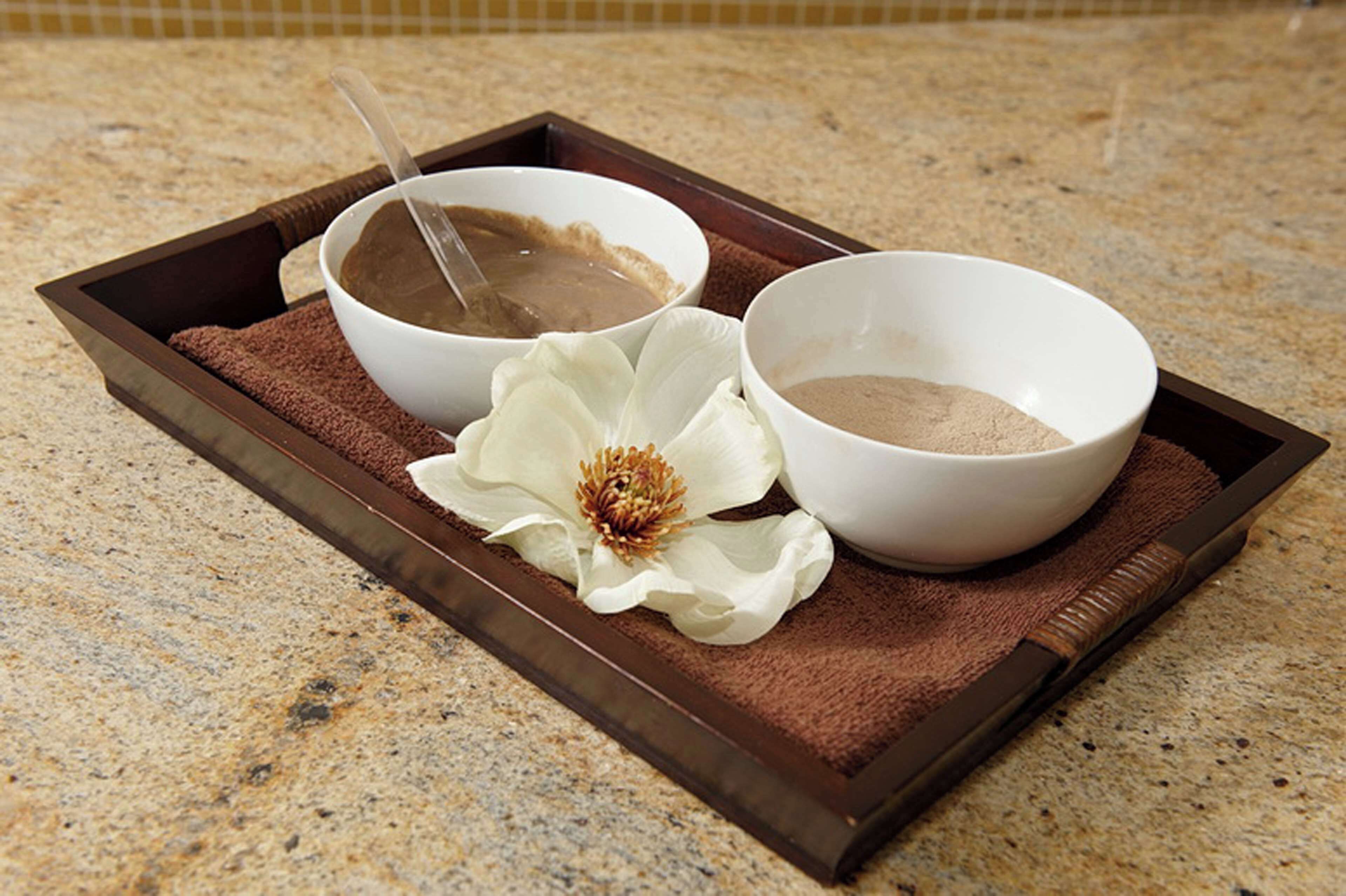 A tray with two bowls of brown liquid and a white flower on a textured surface.
