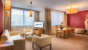 Una camera d'albergo con divano, sedie, un tavolo da pranzo, una TV e una parete decorata di rosso.