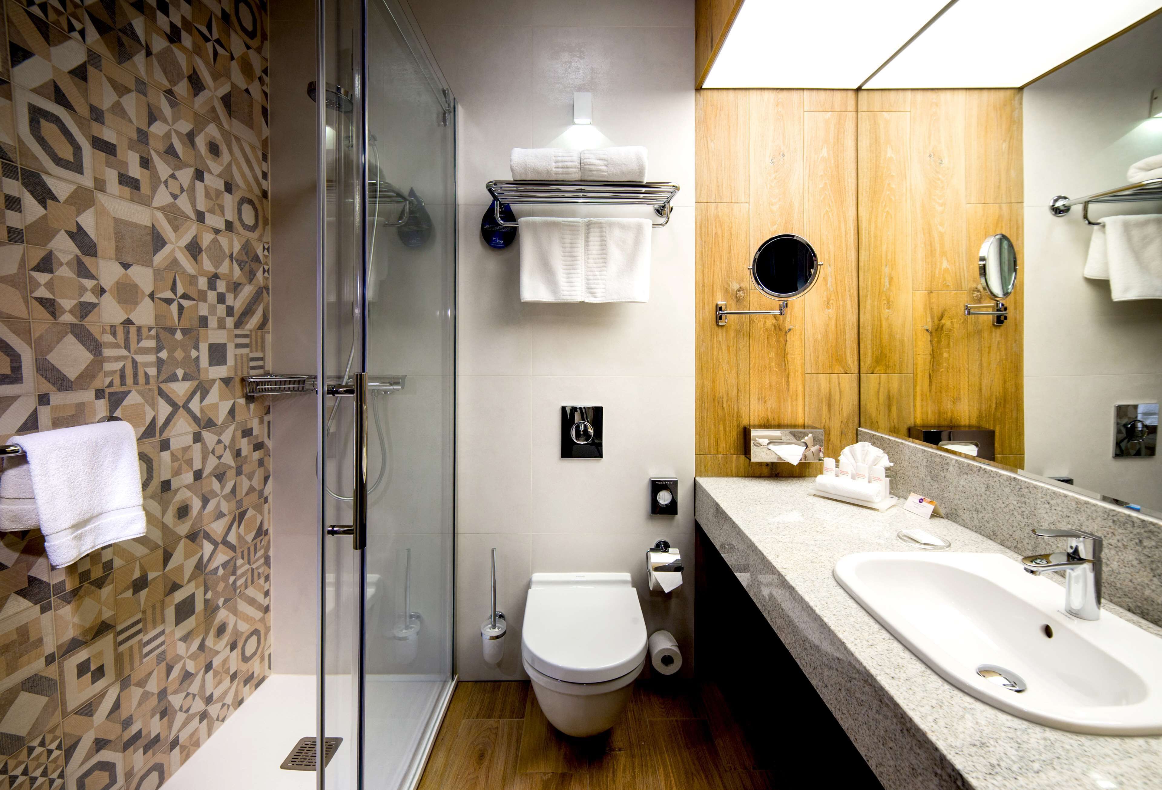 A modern bathroom with a glass shower enclosure, a white toilet, a wooden vanity with a sink, and a large mirror.