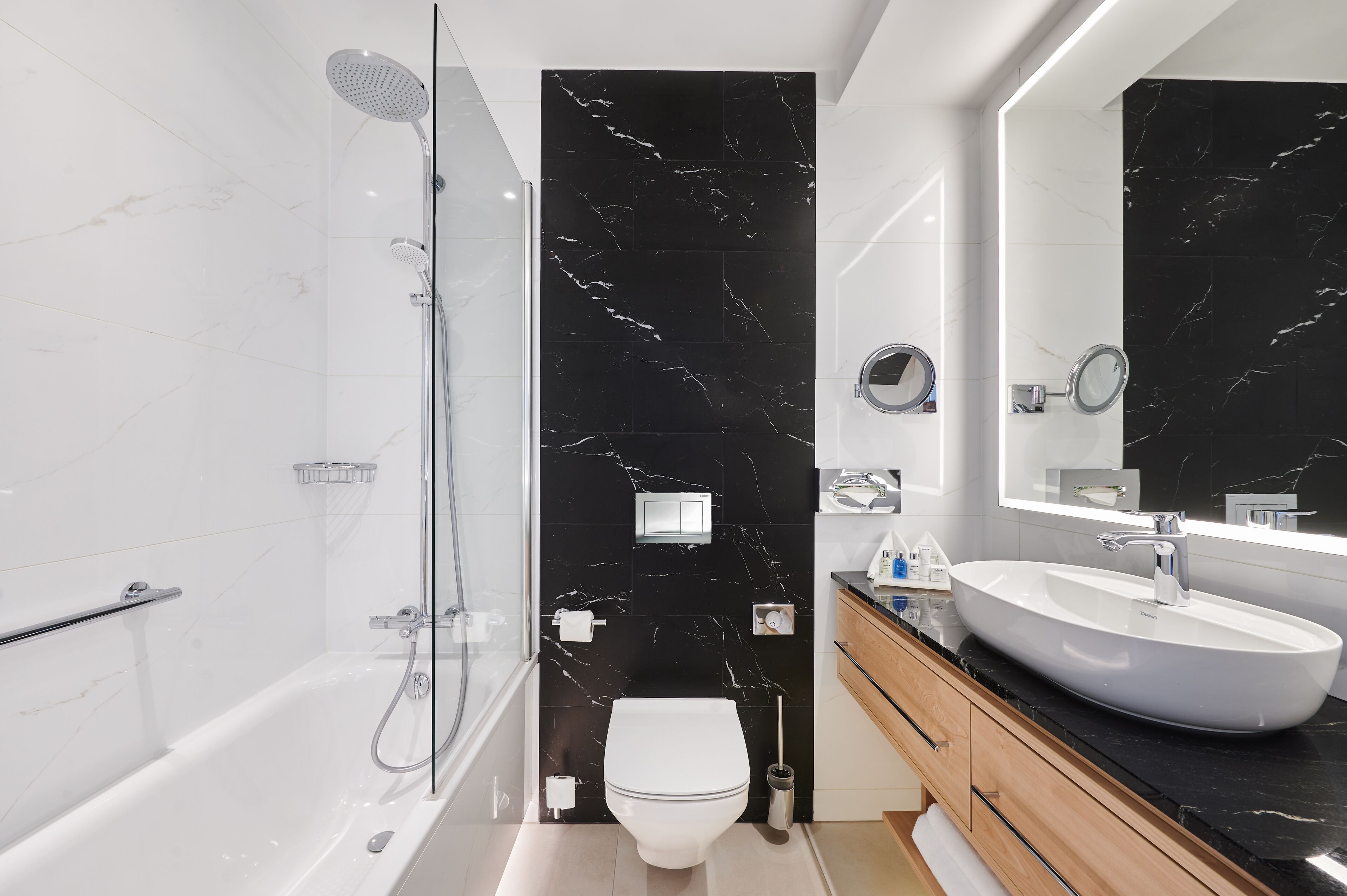 Un baño moderno con ducha de vidrio, inodoro blanco y un amplio lavabo con mueble.