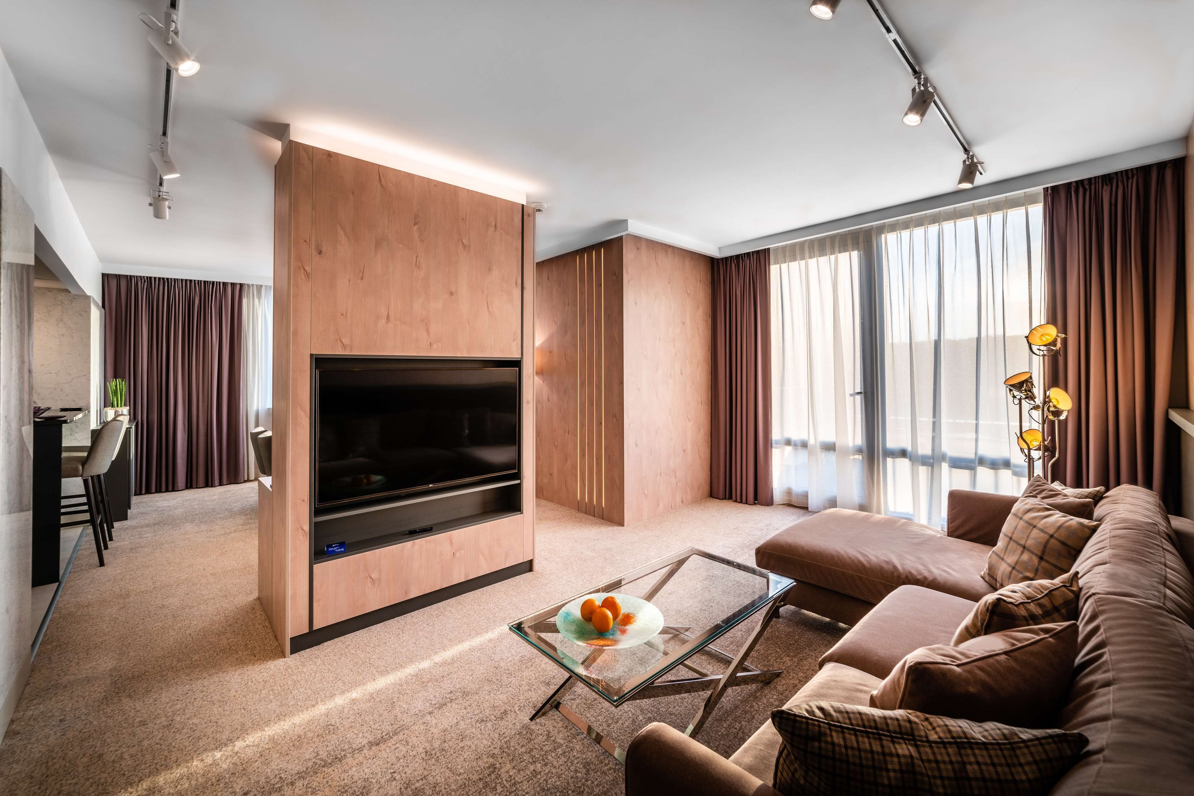 Una sala de estar moderna con una televisión de pantalla plana, una mesa de centro de vidrio, un sofá y un comedor con una silla y una mesita.