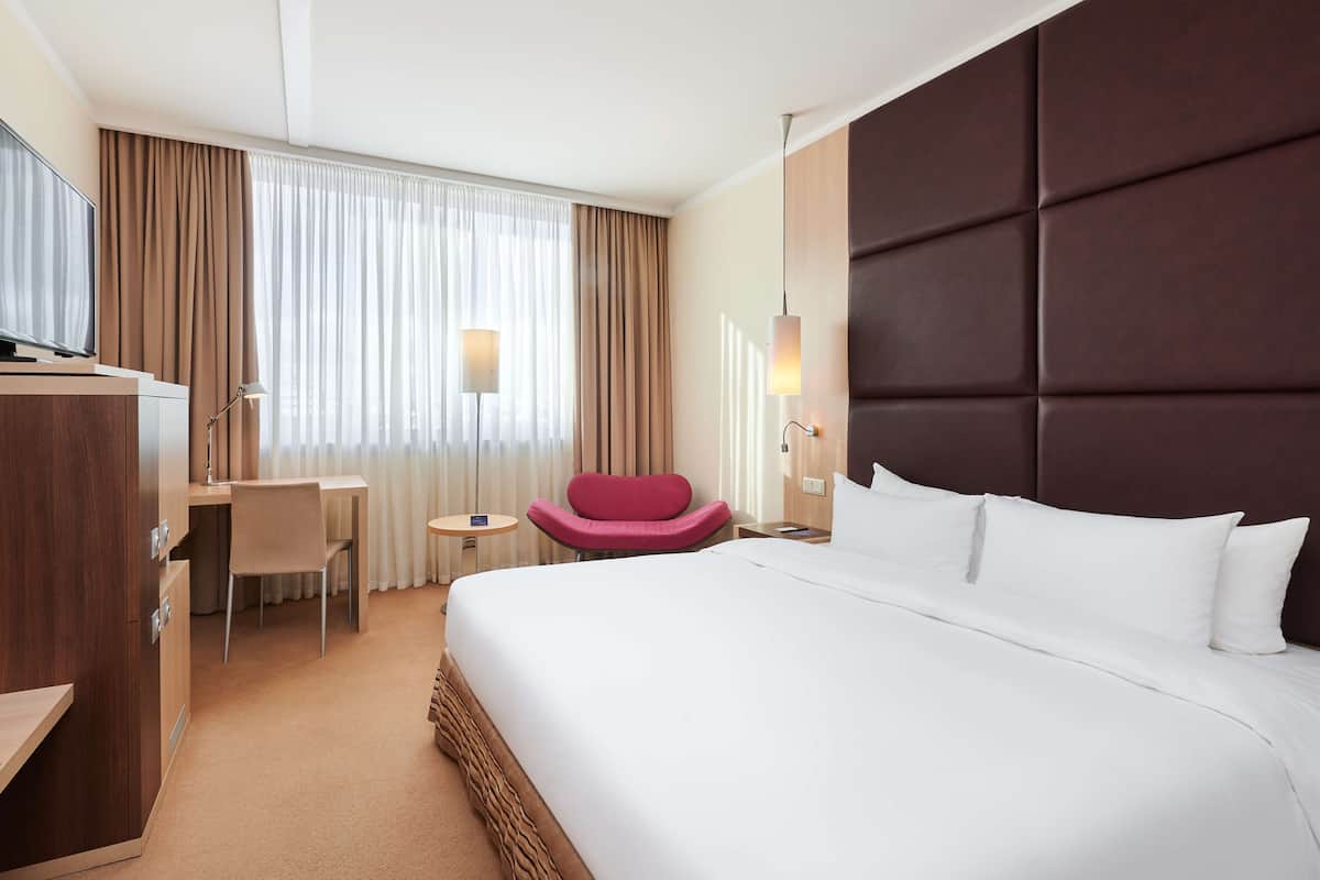 A hotel room with a large bed, a desk, a chair, and a TV.