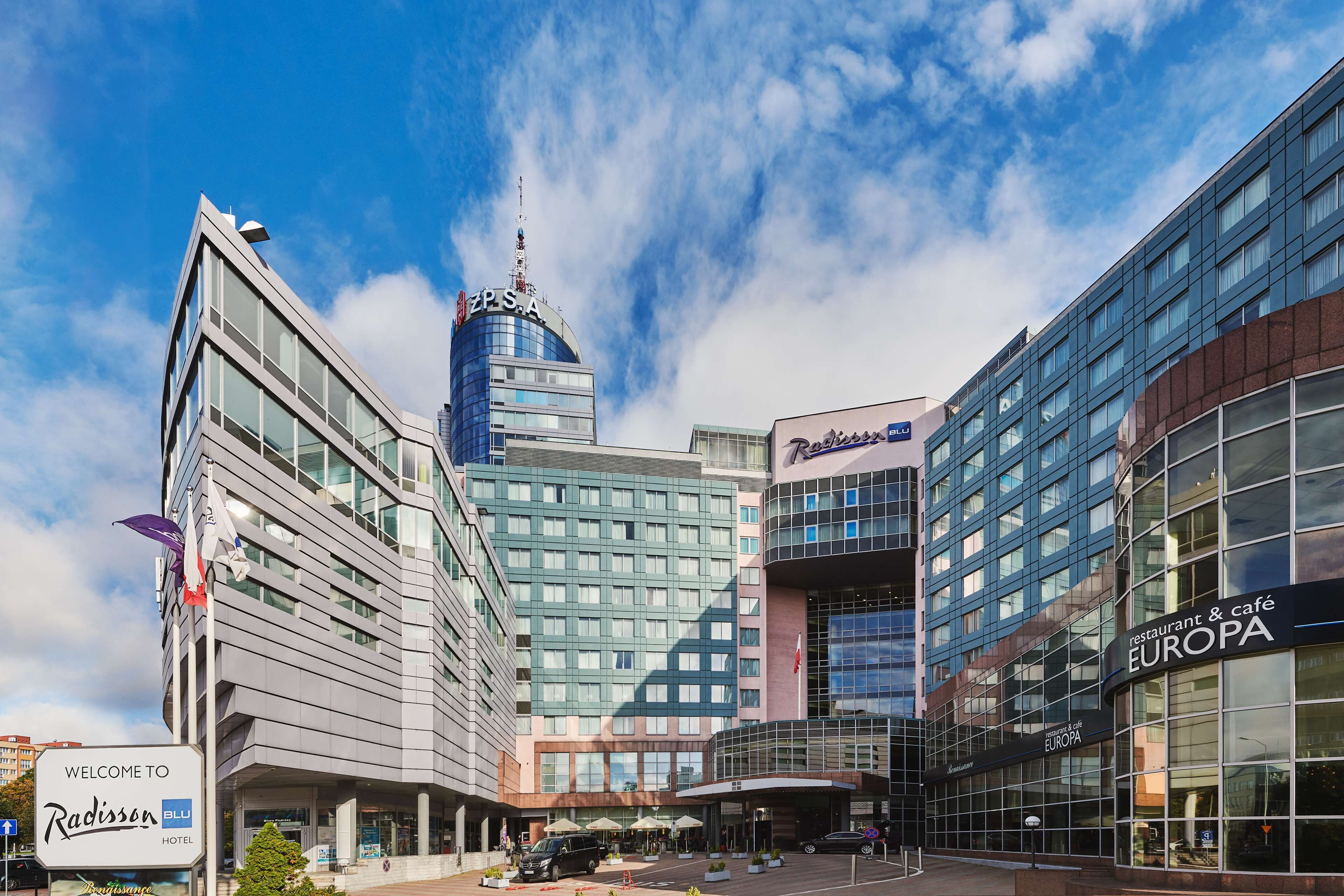 A Radisson Blu hotel with a modern glass facade, a prominent ZPSA building in the background, and a Europa restaurant & café.