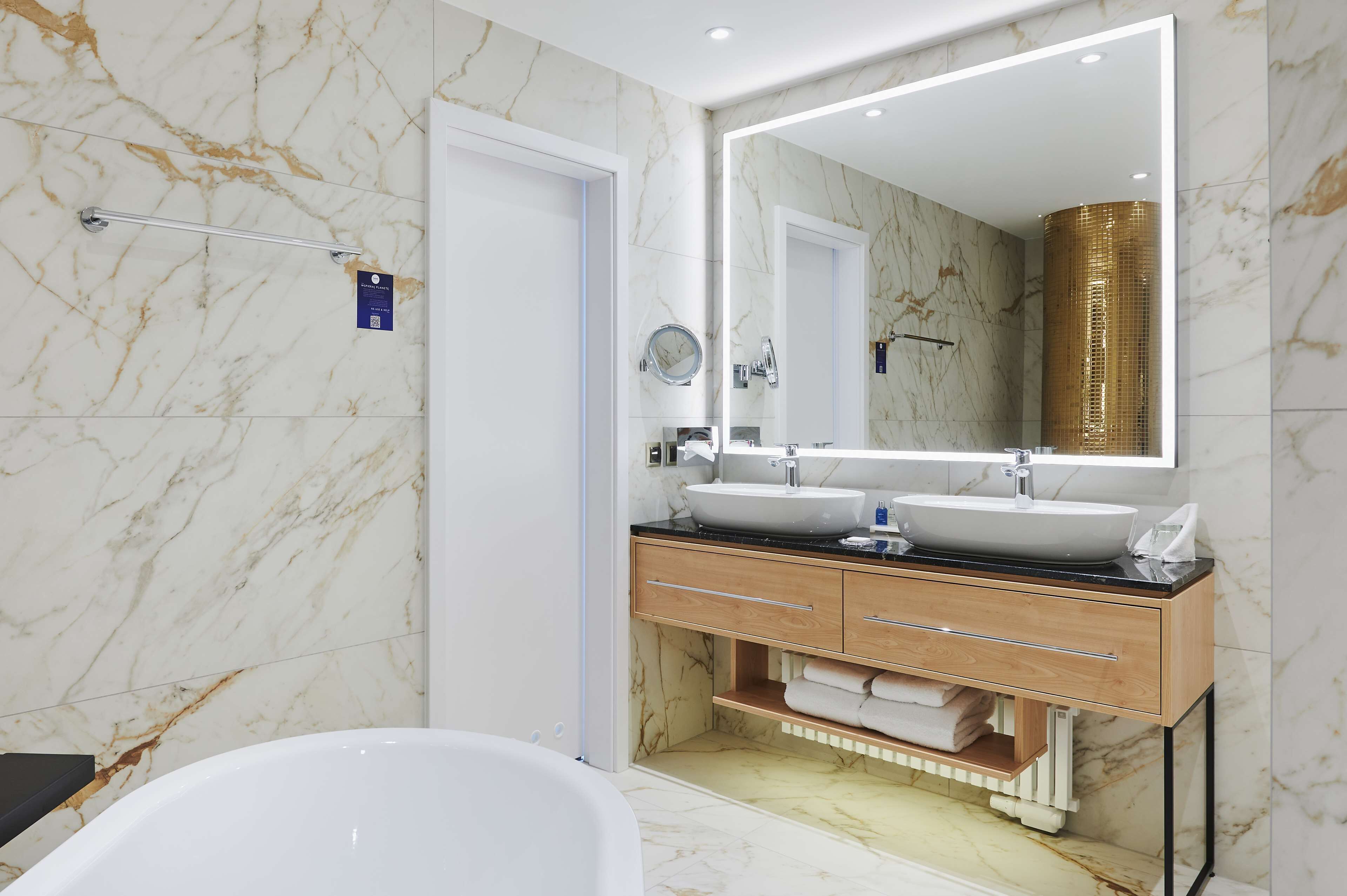Ein modernes Badezimmer mit Marmorwänden, einem Doppelwaschtisch, einem großen Spiegel und einer Badewanne.