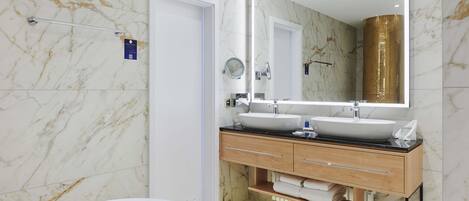 Ein modernes Badezimmer mit Marmorwänden, einem Doppelwaschtisch, einem großen Spiegel und einer Badewanne.