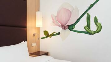 A hotel room with a bed, a nightstand, a wall-mounted lamp, and a floral mural.