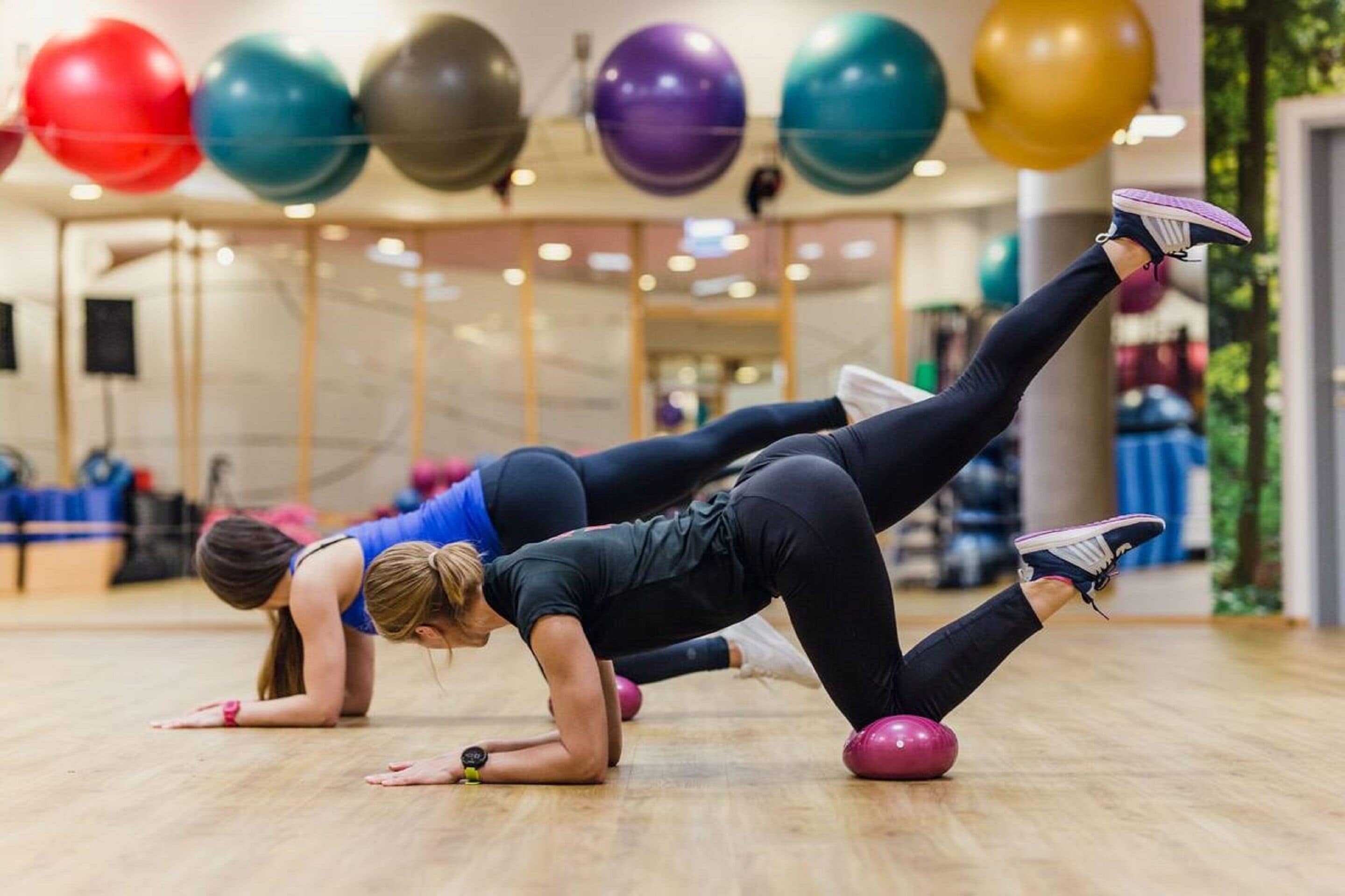 Dos personas ejercitándose con balones de gimnasia en un gimnasio.