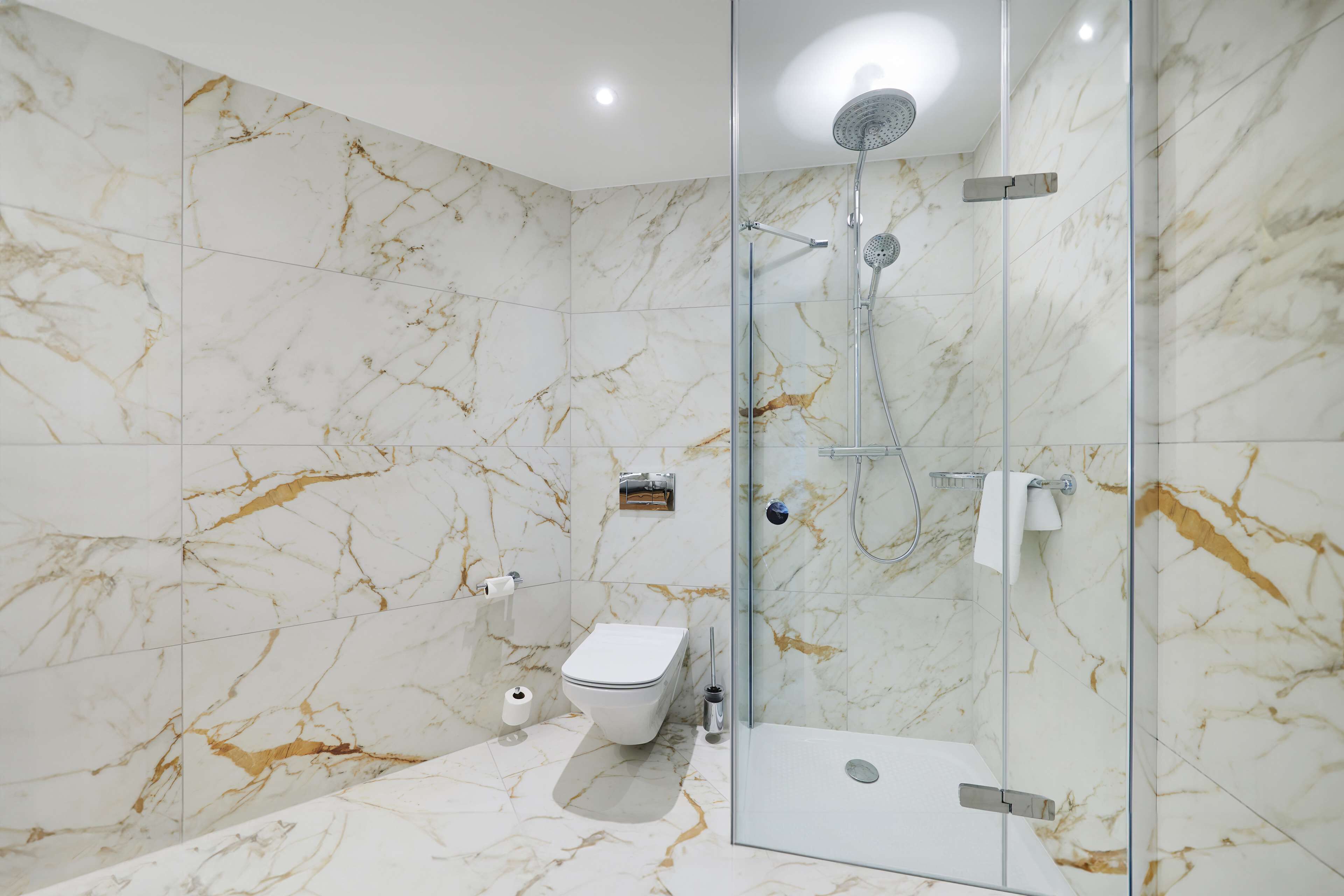 Un baño moderno con ducha de vidrio, inodoro y paredes de mármol.