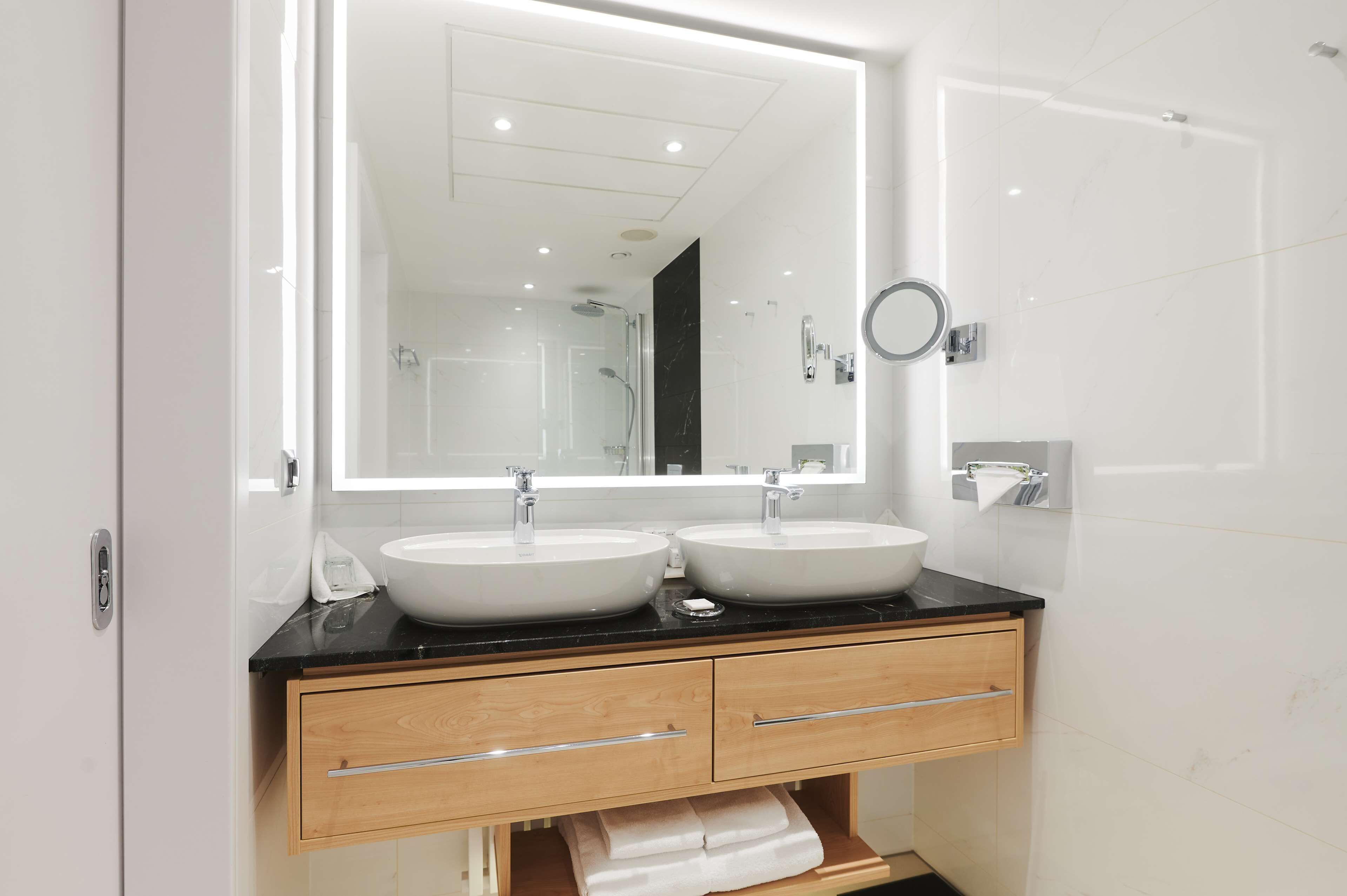 Ein modernes Badezimmer mit zwei Waschbecken, einem großen Spiegel und einem Handtuchhalter.