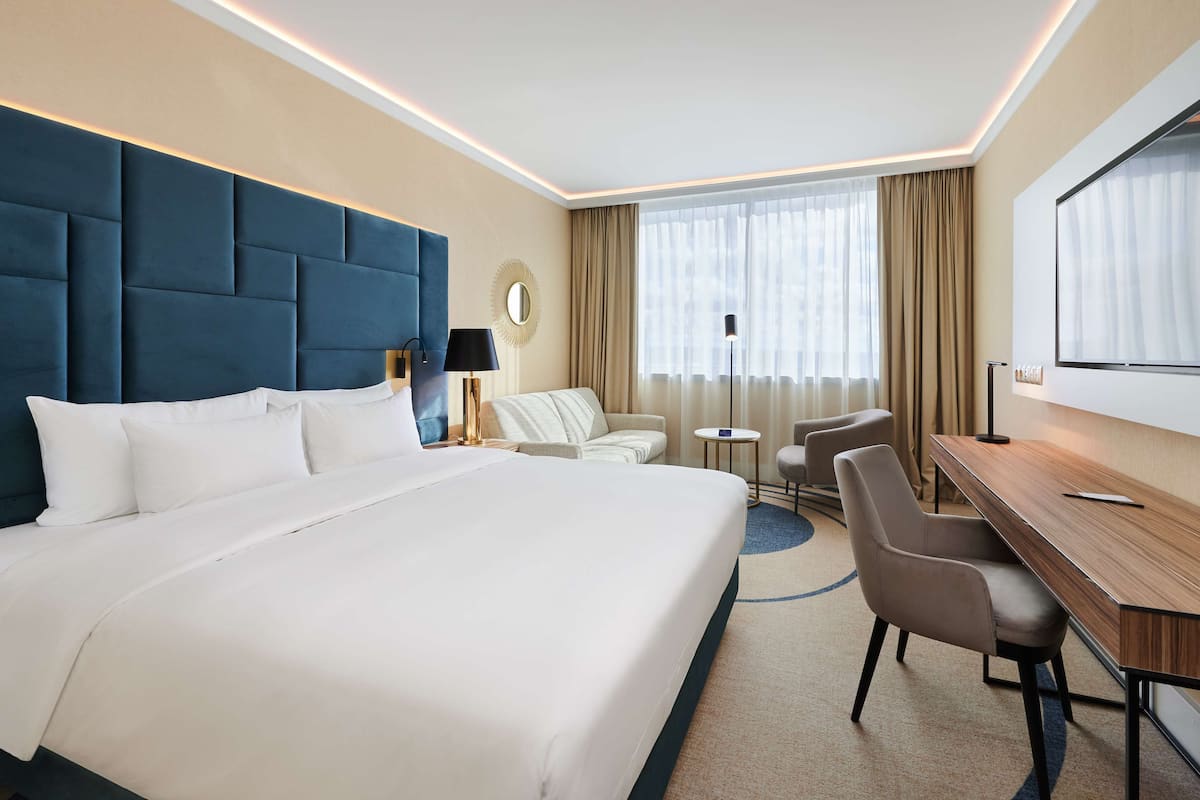 A hotel room with a large bed, a desk, a chair, a round mirror, and a TV.
