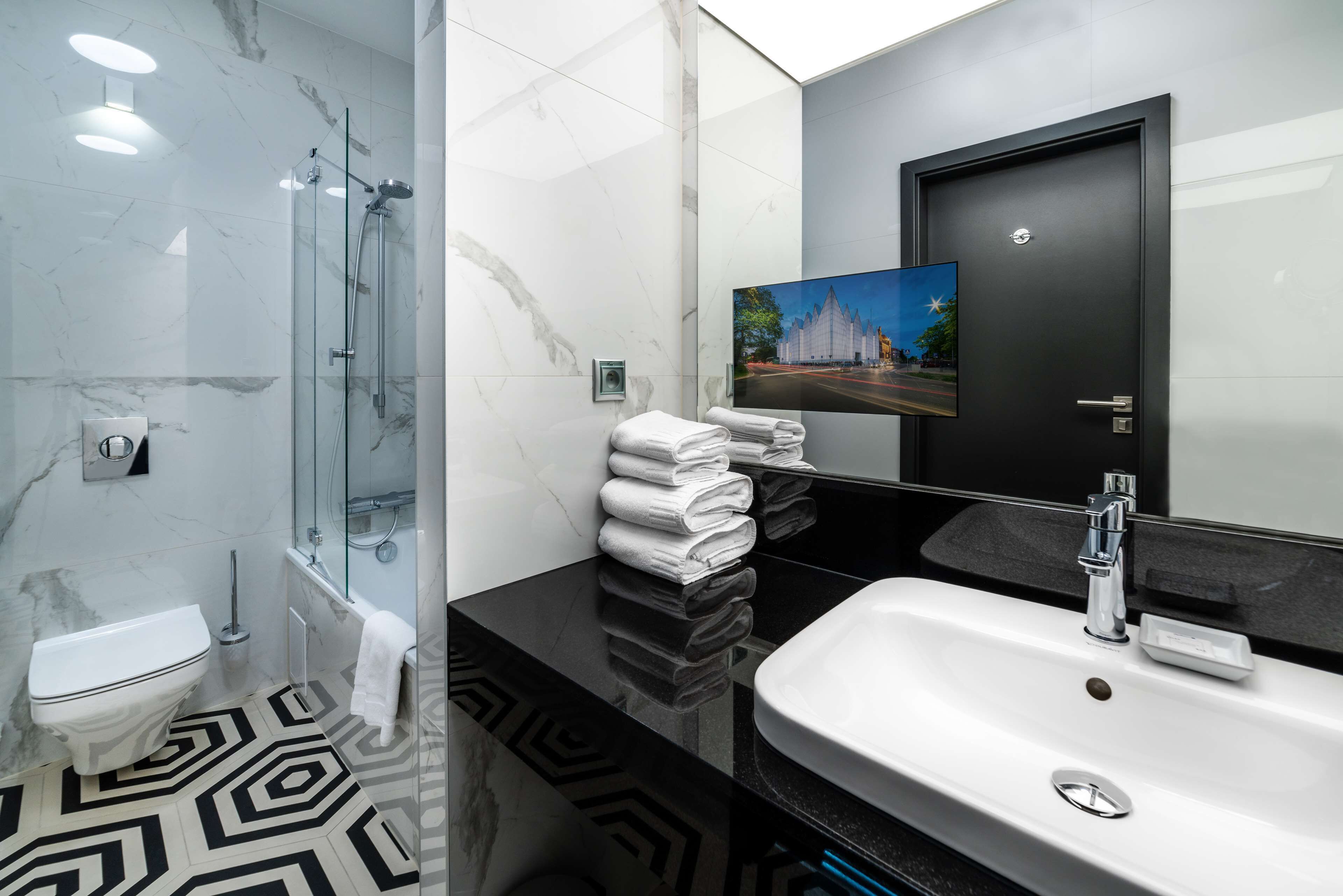 Un baño moderno con ducha de vidrio, lavamanos blanco y encimera negra.
