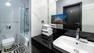 Un baño moderno con ducha de vidrio, lavamanos blanco y encimera negra.