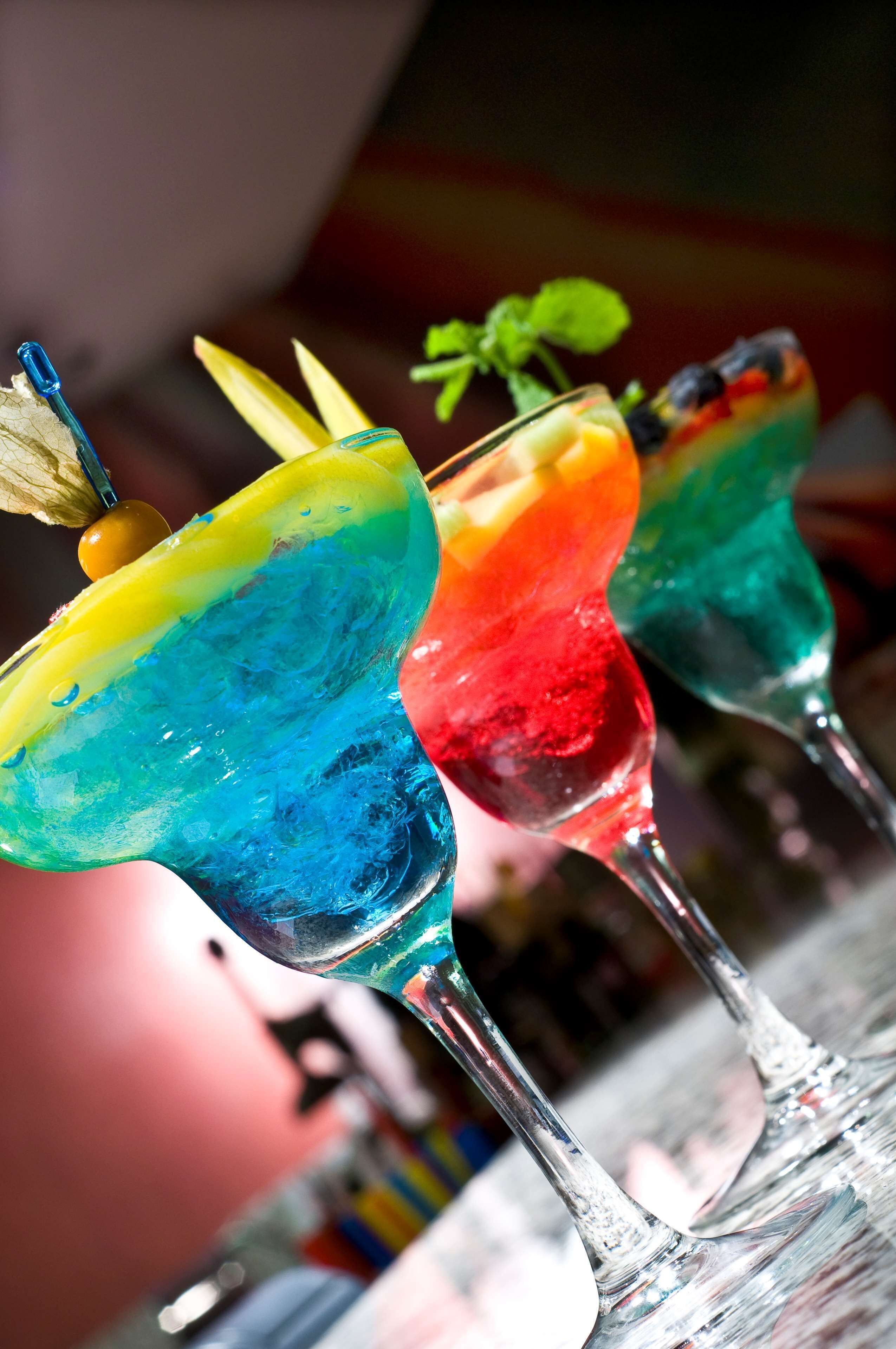 Three colorful cocktails in glasses with a mint garnish.