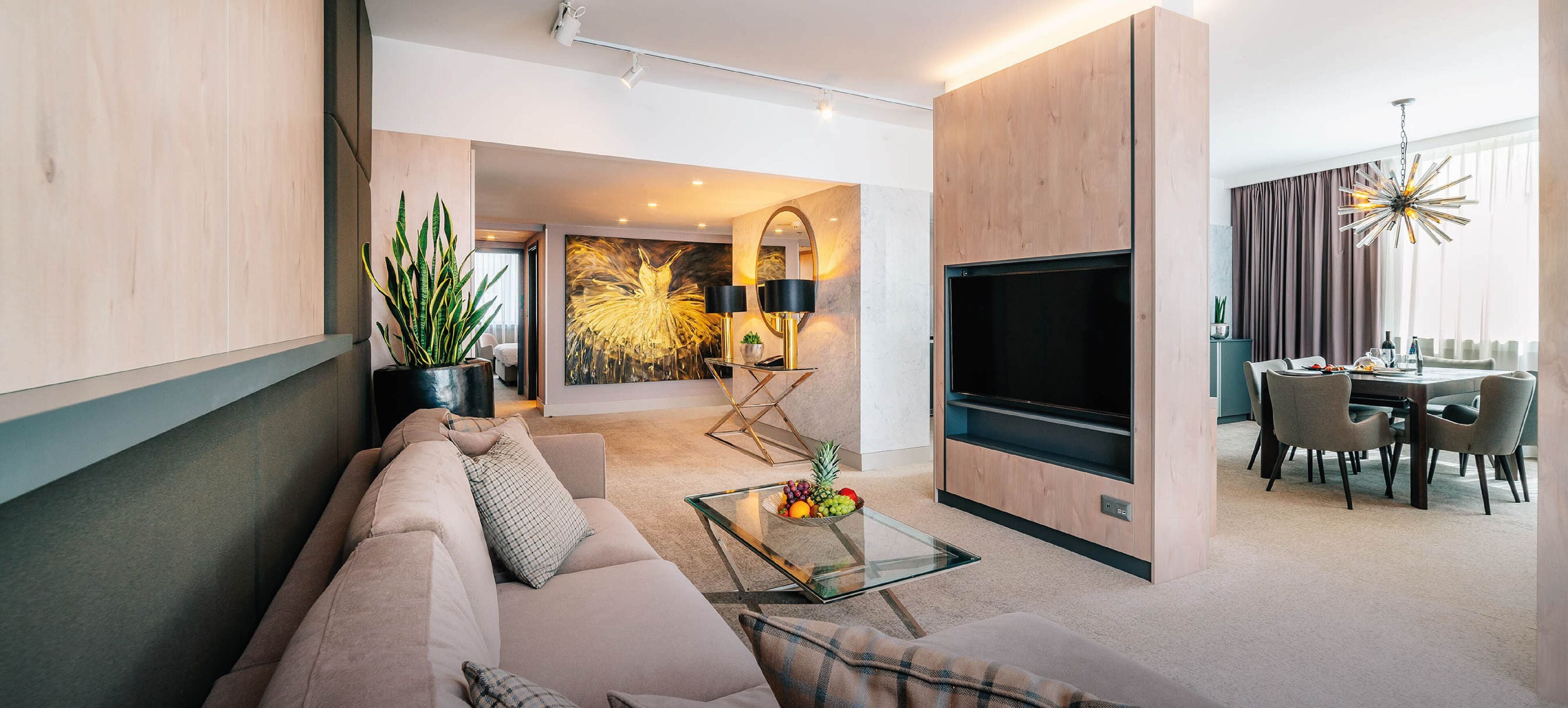 Una sala de estar moderna con sofá, mesa de centro y televisor de pantalla plana. Al fondo, un comedor con mesa y sillas.