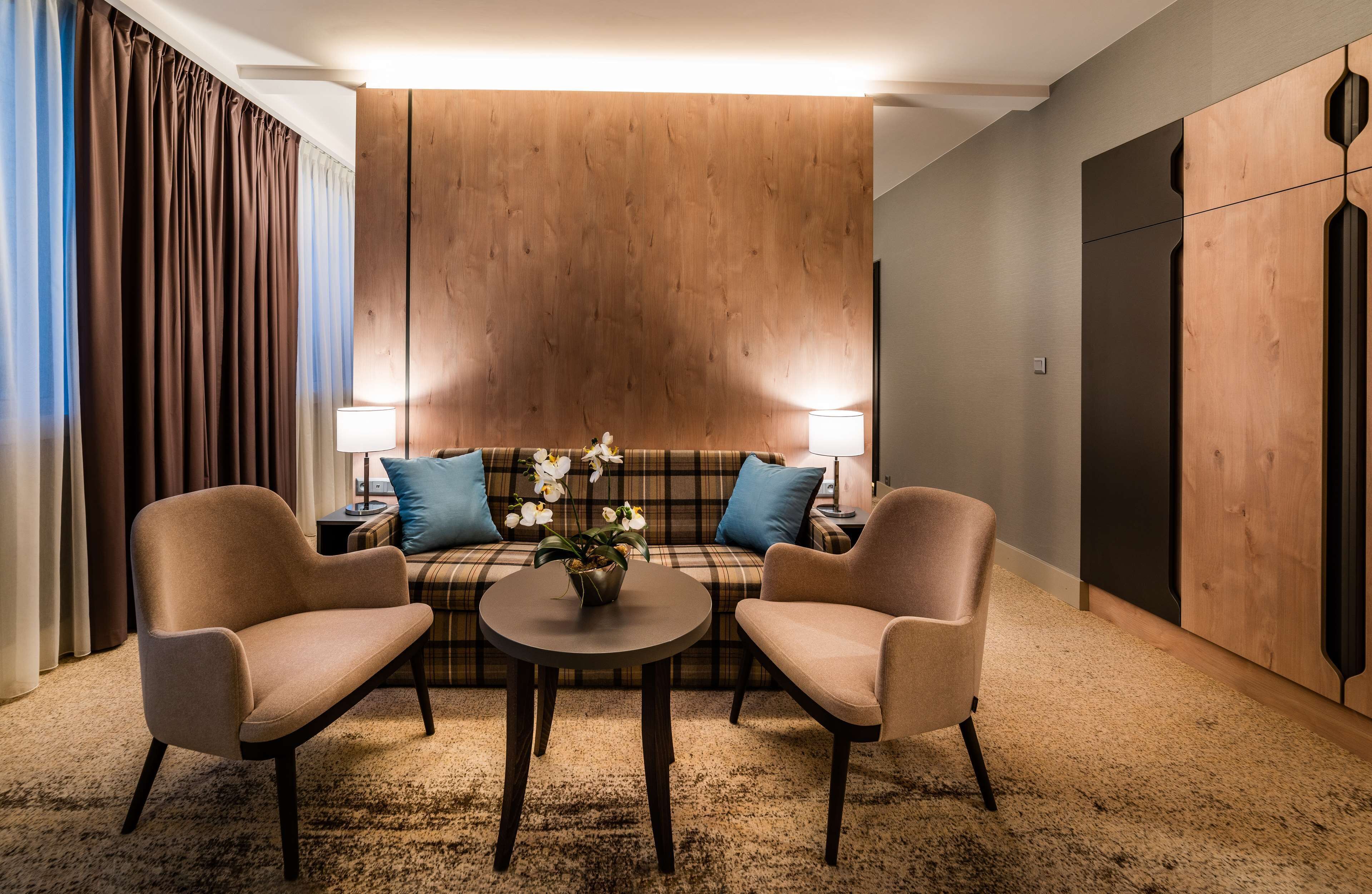 A modern room with a sofa, two armchairs, a small table, and a lamp.