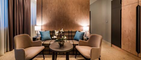 A modern room with a sofa, two armchairs, a small table, and a lamp.