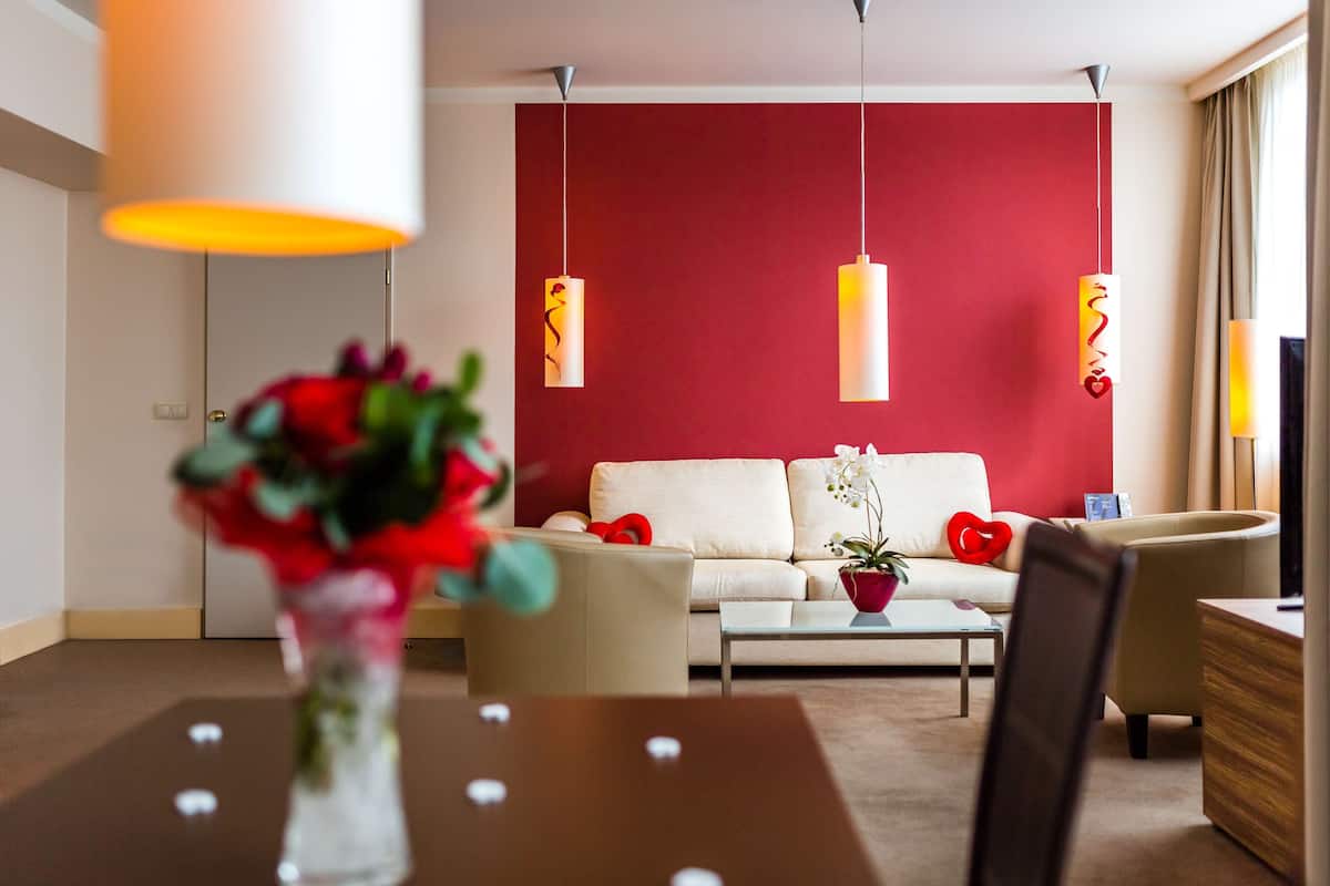 A modern living room with a red accent wall, a white sofa, a coffee table, and hanging pendant lights.