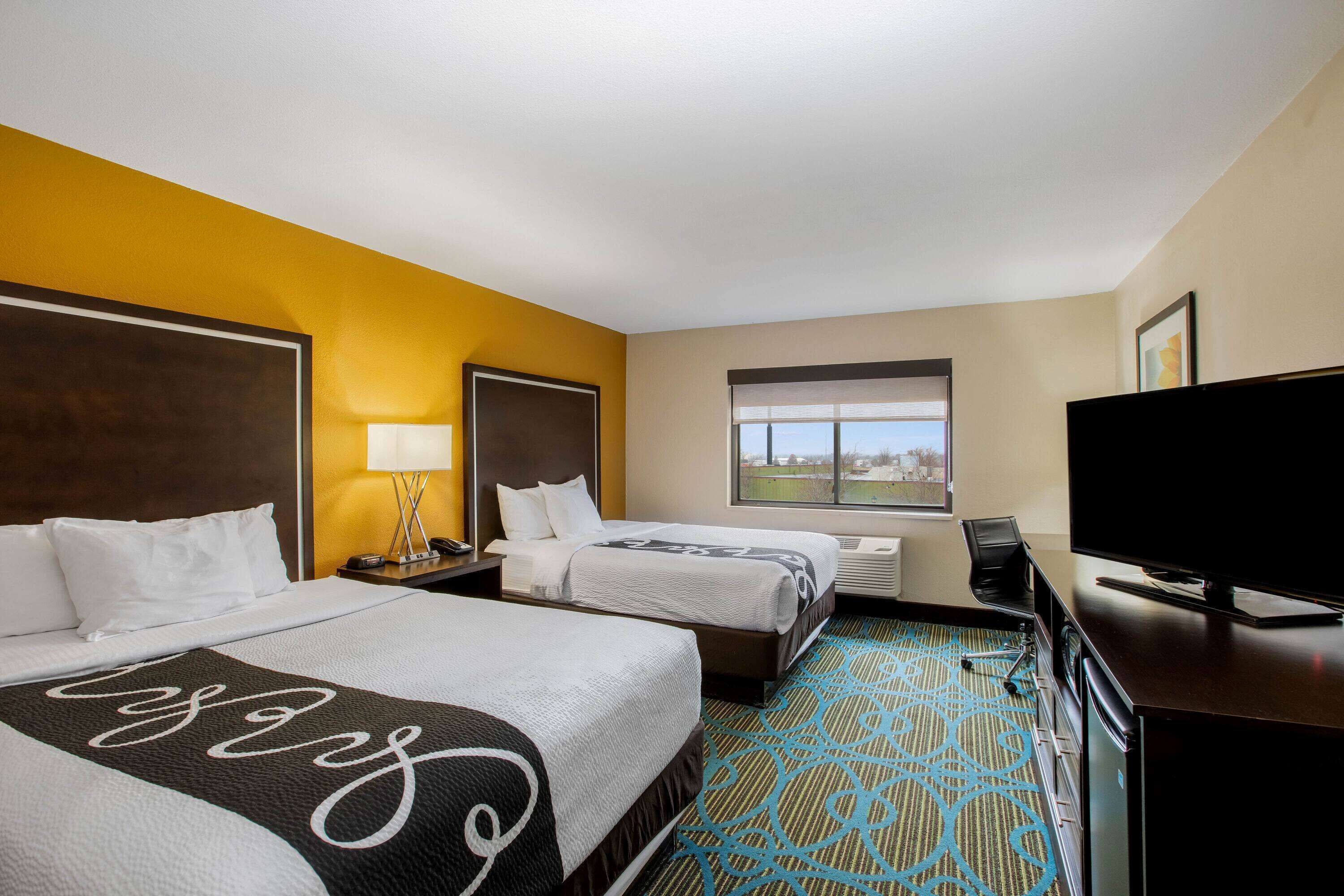 A hotel room with two beds, a TV, a desk, and a window with a city view.