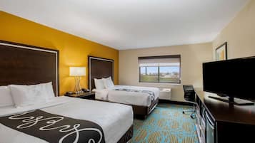 A hotel room with two beds, a TV, a desk, and a window with a city view.