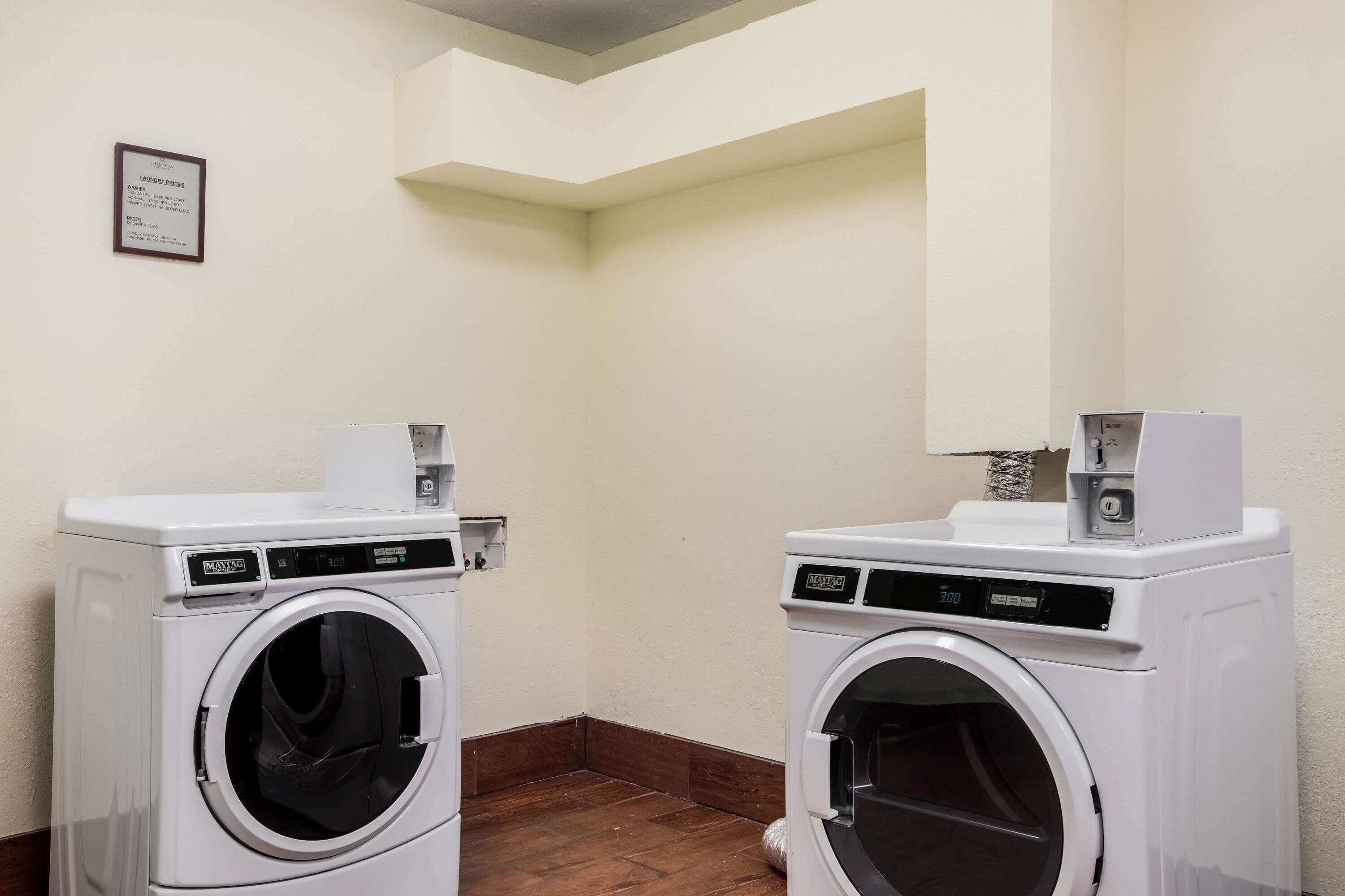 A laundry room with two white front-loading washing machines, a plaque on the wall, and wooden flooring.