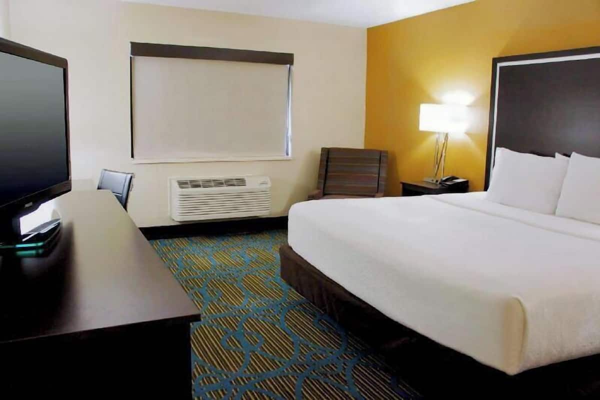 Ein Hotelzimmer mit Bett, Schreibtisch, Fernseher, Klimaanlage, Lampe und Fenster.