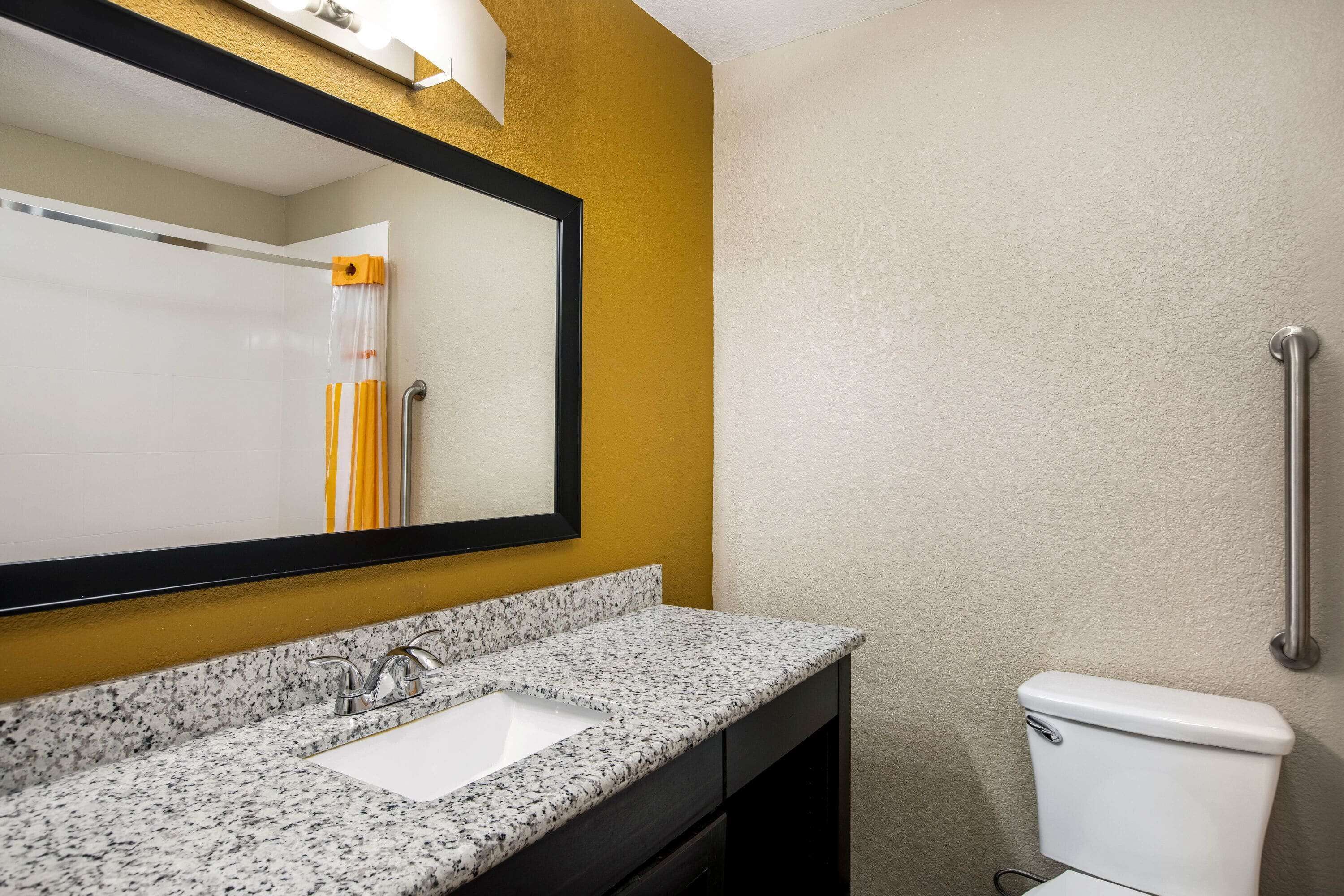 A bathroom with a granite countertop sink, a white toilet, and a mirror with a black frame.