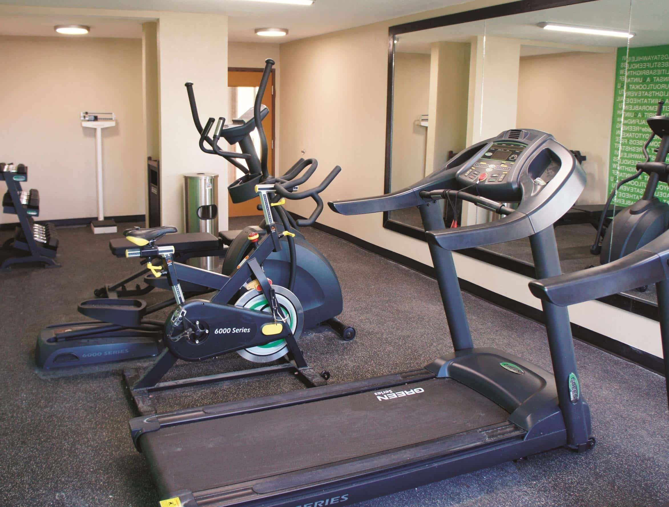 Un gimnasio con cintas de correr, bicicletas estáticas y un espejo grande.