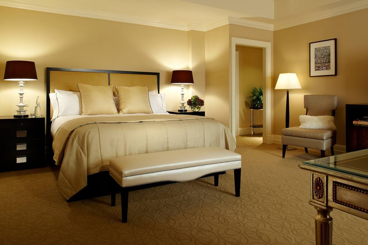 A hotel room with a large bed, bedside lamps, a television, a chair, and a small table with a decorative item.