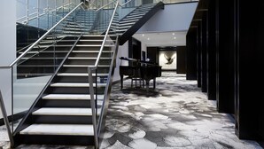A modern interior with a glass staircase, a grand piano, and a patterned floor.