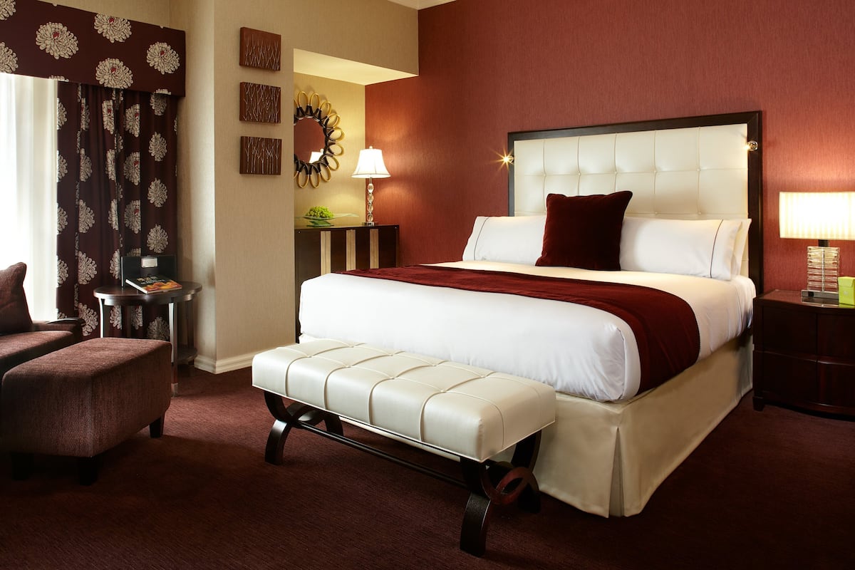 A hotel room with a large bed, a chair, a nightstand, and a lamp.