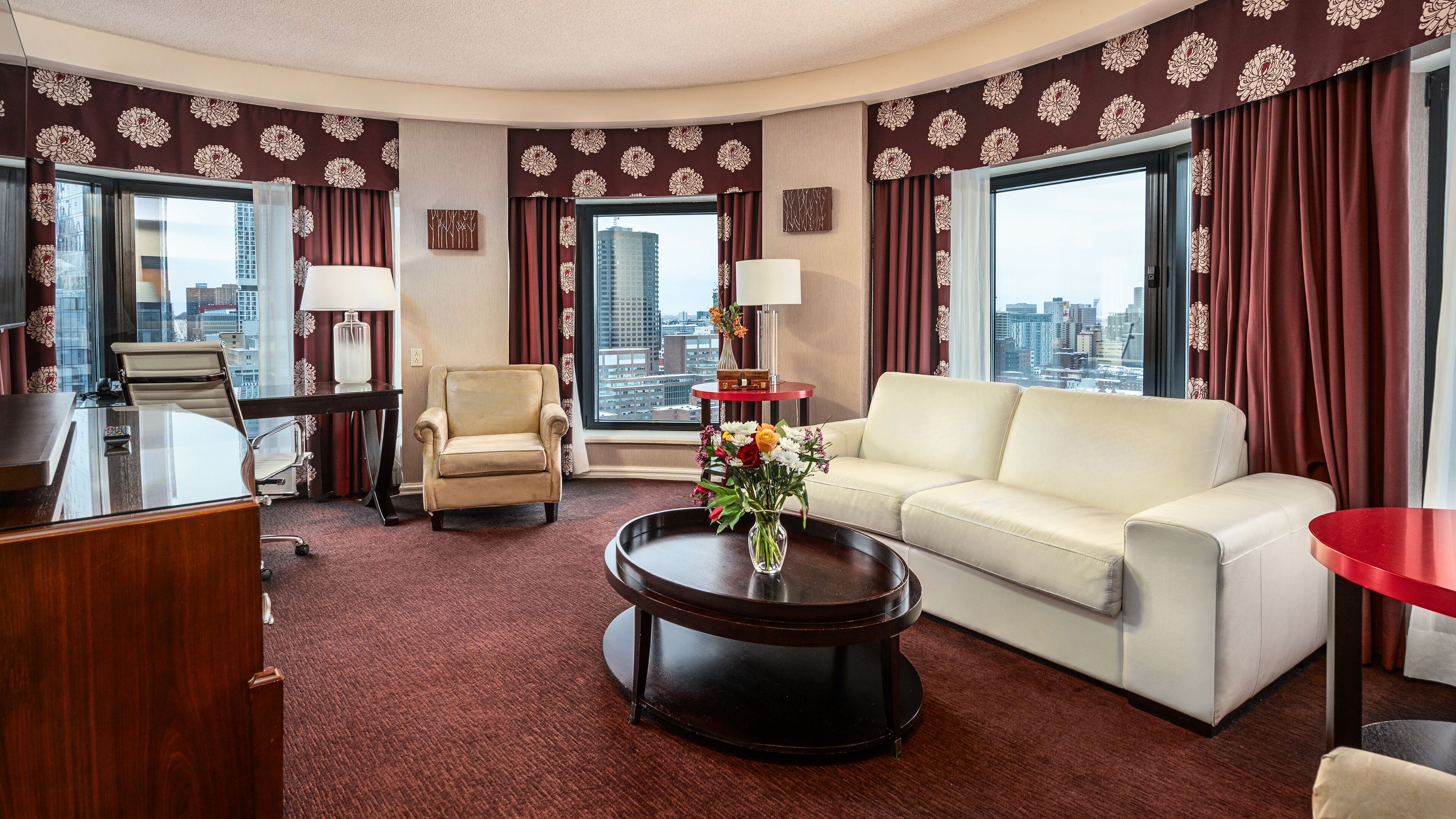 A hotel room with a sofa, armchair, desk, and coffee table.