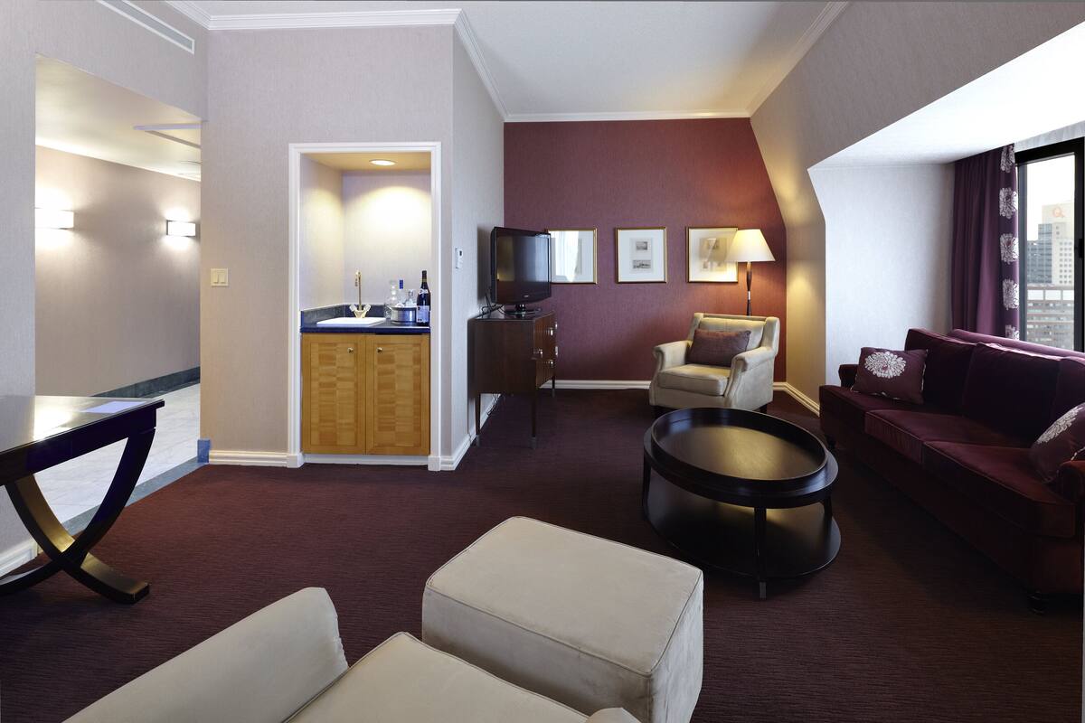 A hotel room with a seating area, a television, a small table, and a view of the city.
