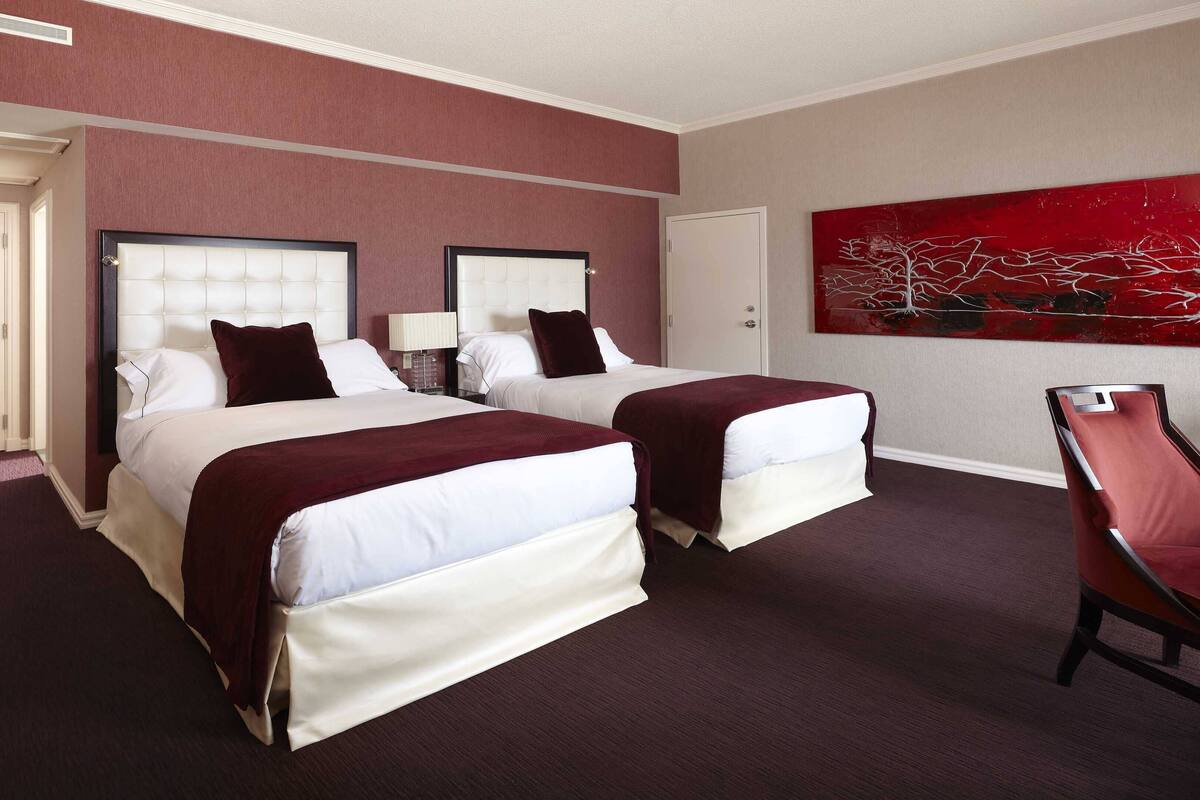 A hotel room with two beds, a red chair, and a red abstract painting on the wall.