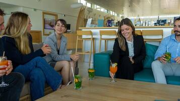 A group of people seated at a wooden table in a modern interior with a bar area in the background.