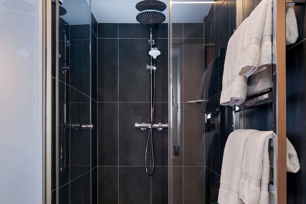 Un baño moderno con ducha de vidrio, baldosas oscuras y un perchero con toallas dobladas.