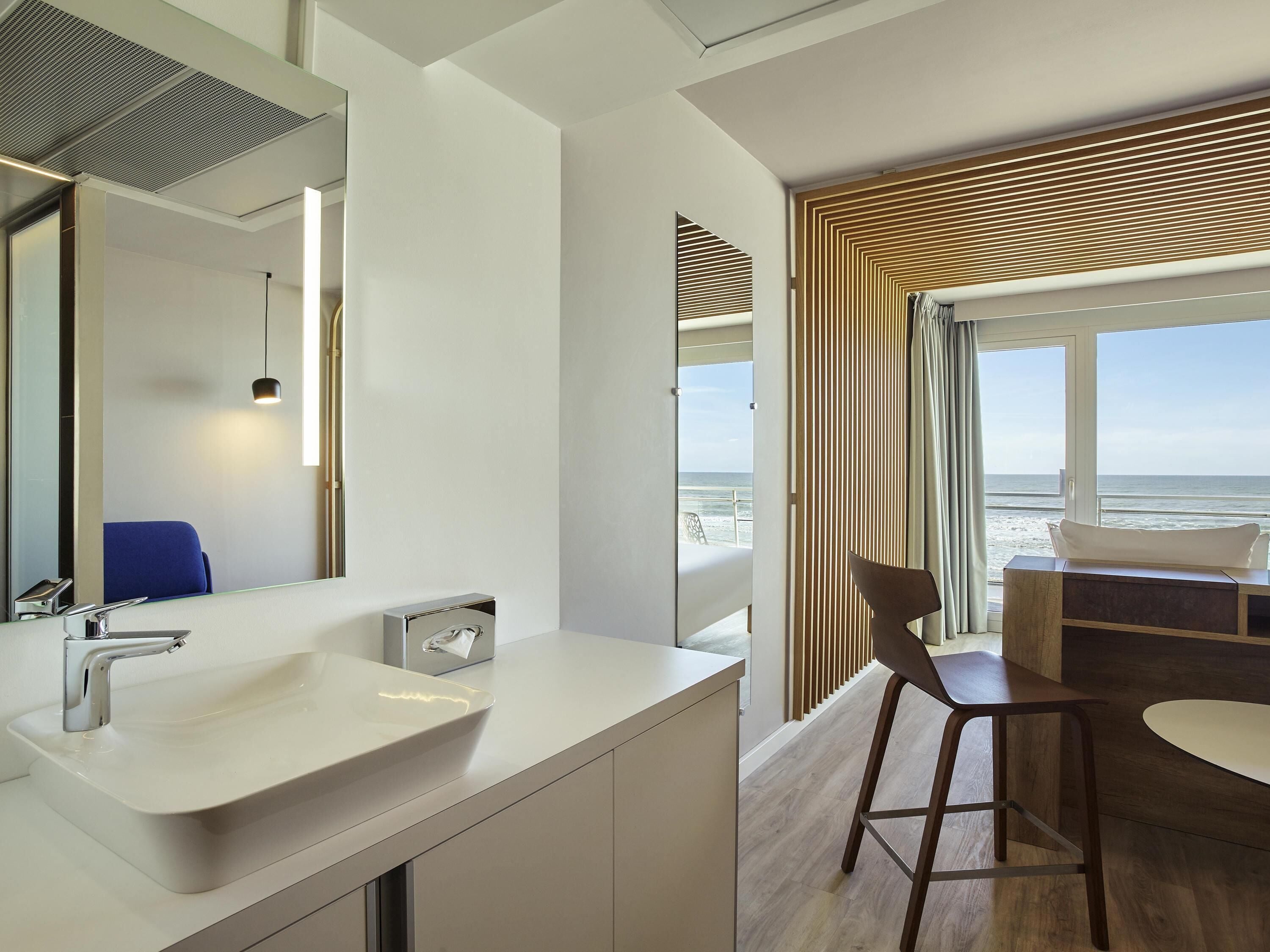 Une salle de bain moderne avec un grand miroir, un lavabo blanc et une fenêtre à cadre en bois.