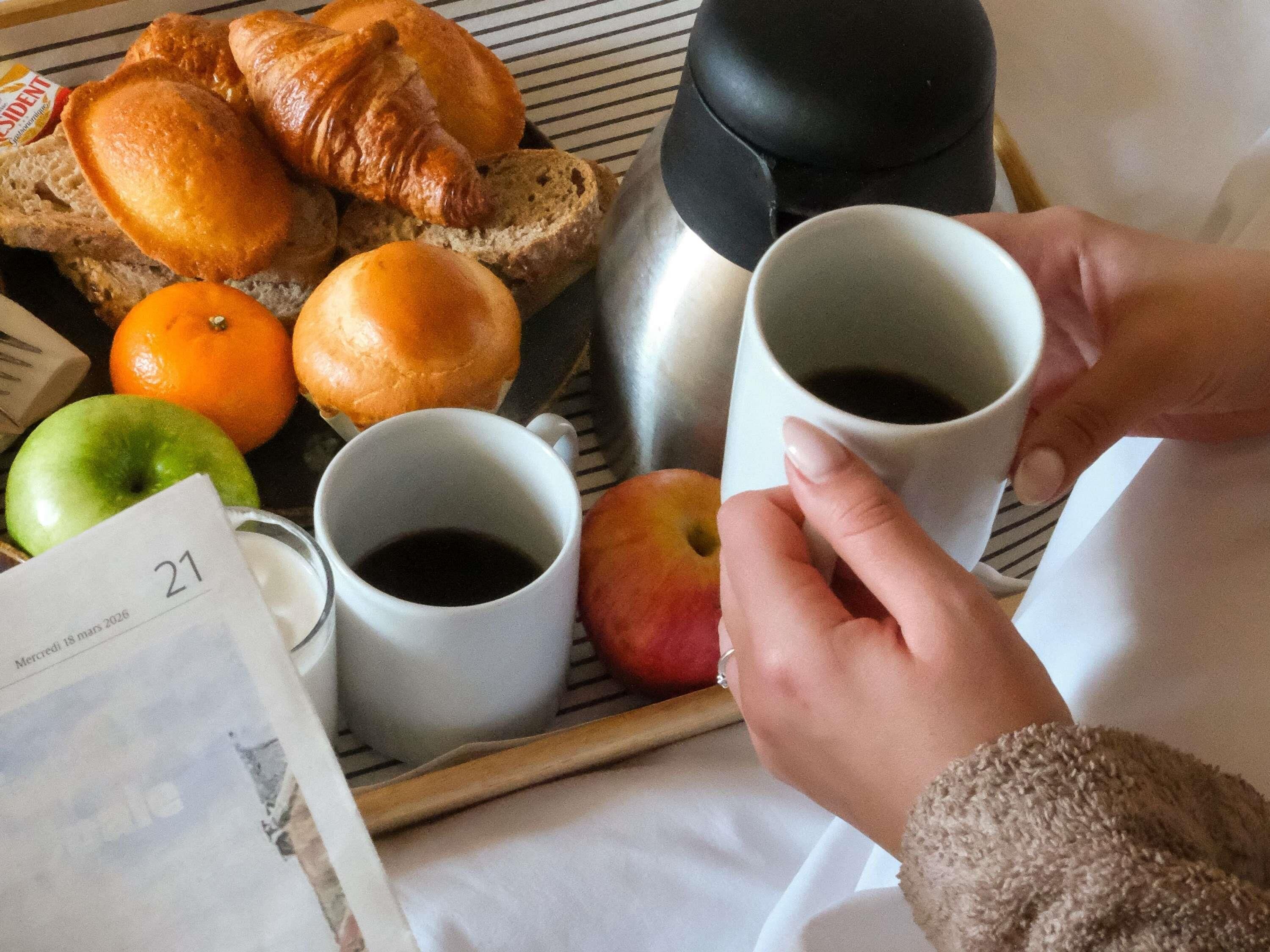 Un plateau contenant des croissants, du pain, des oranges et une pomme, accompagné de deux tasses de café.