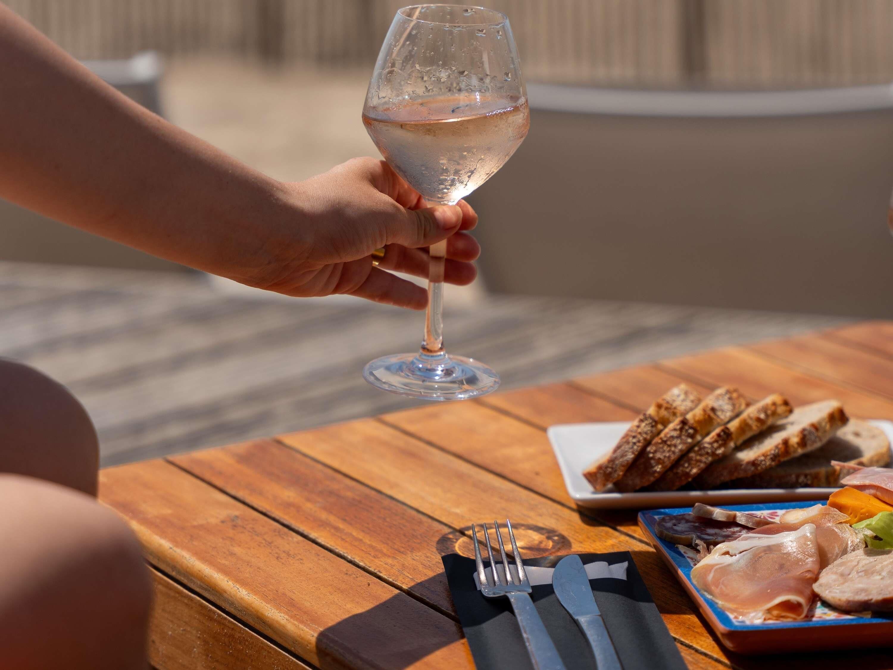 Une table en bois sur laquelle se trouve une assiette de charcuterie, un verre de vin blanc et une serviette avec des couverts.