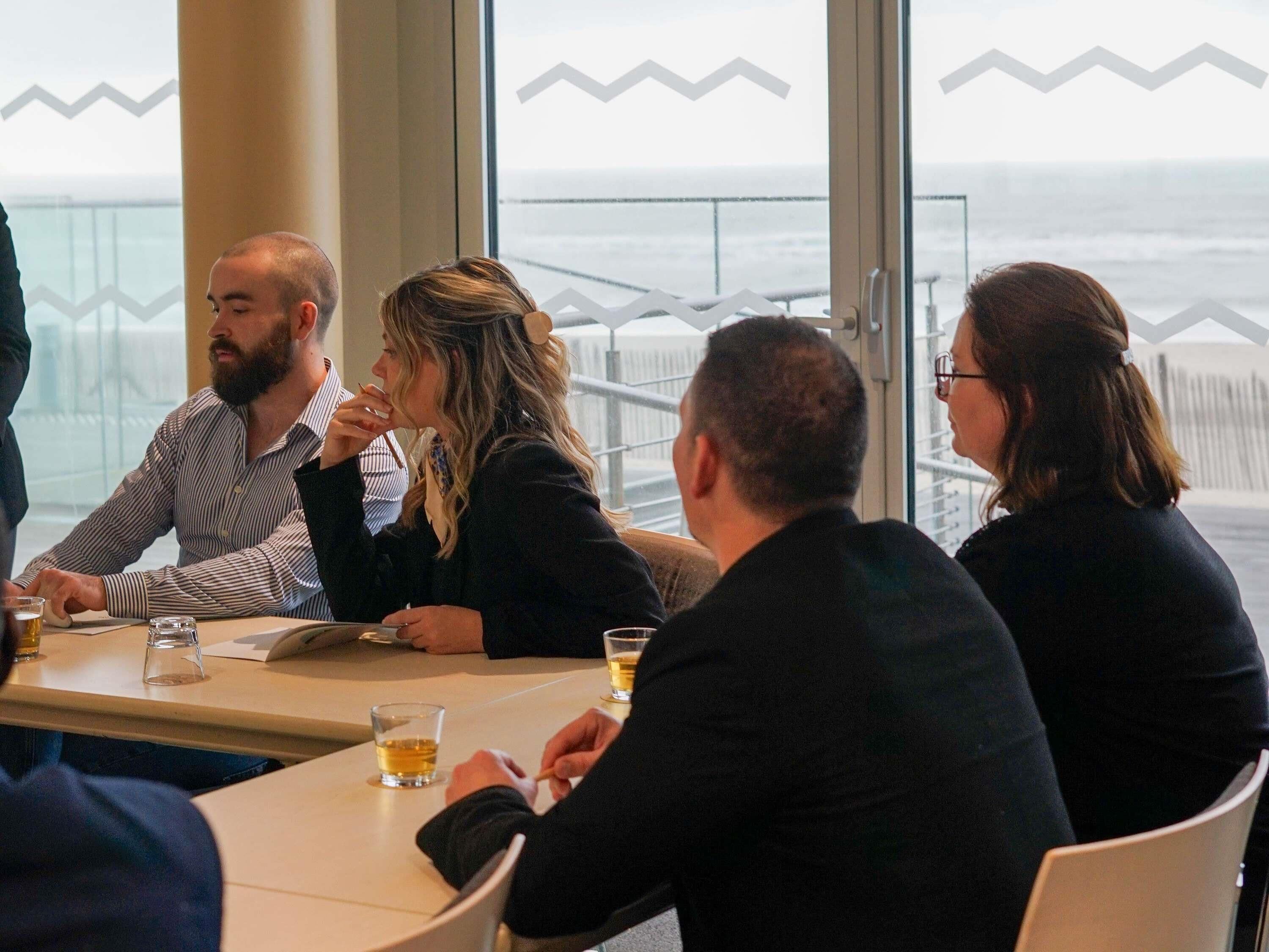 A group of people seated at a table with a view of the ocean through large windows.