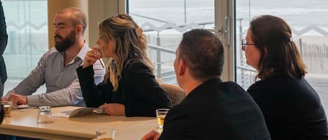 A group of people seated at a table with a view of the ocean through large windows.