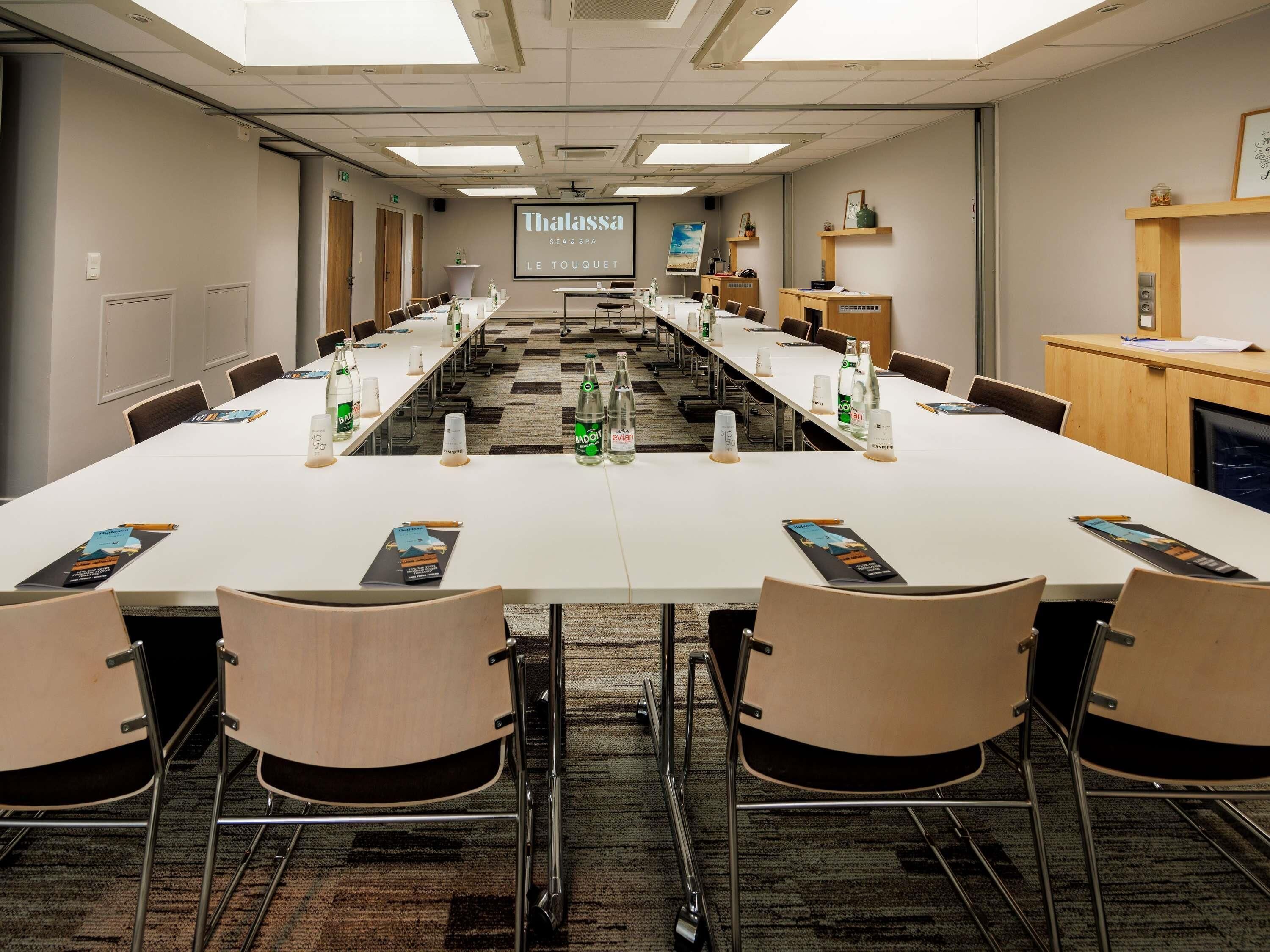 A conference room with a long table, chairs, water bottles, and a projector screen displaying 'Thalassa SEA&SPA LE TOUQUET'.